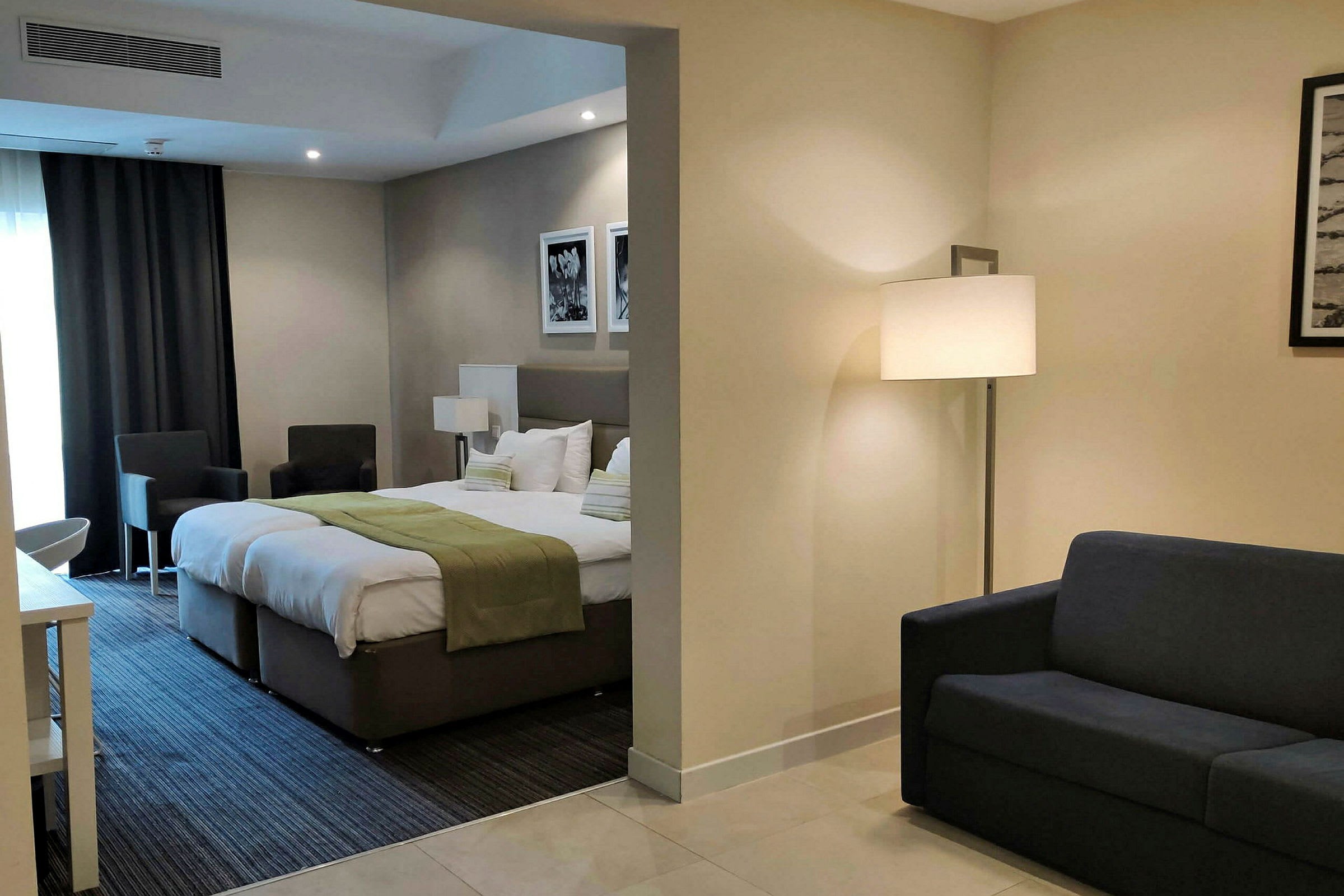 Ett hotellrum med en säng, grönt överkast, sittmöbler och en soffa i separat del. (AI-genererad text)