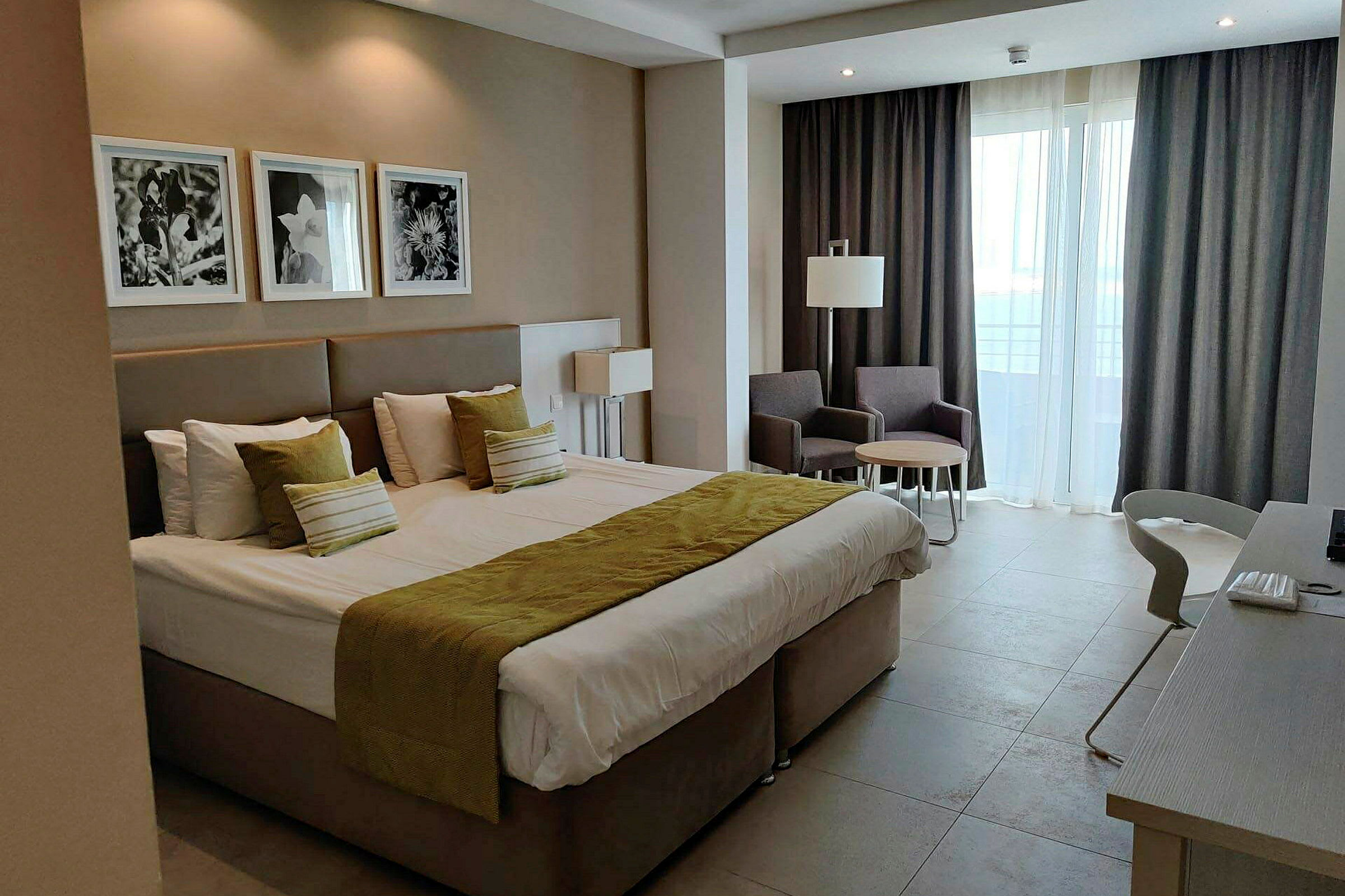Hotellrum med en stor säng, två fåtöljer med ett bord och fönster med gardiner. (AI-genererad text)