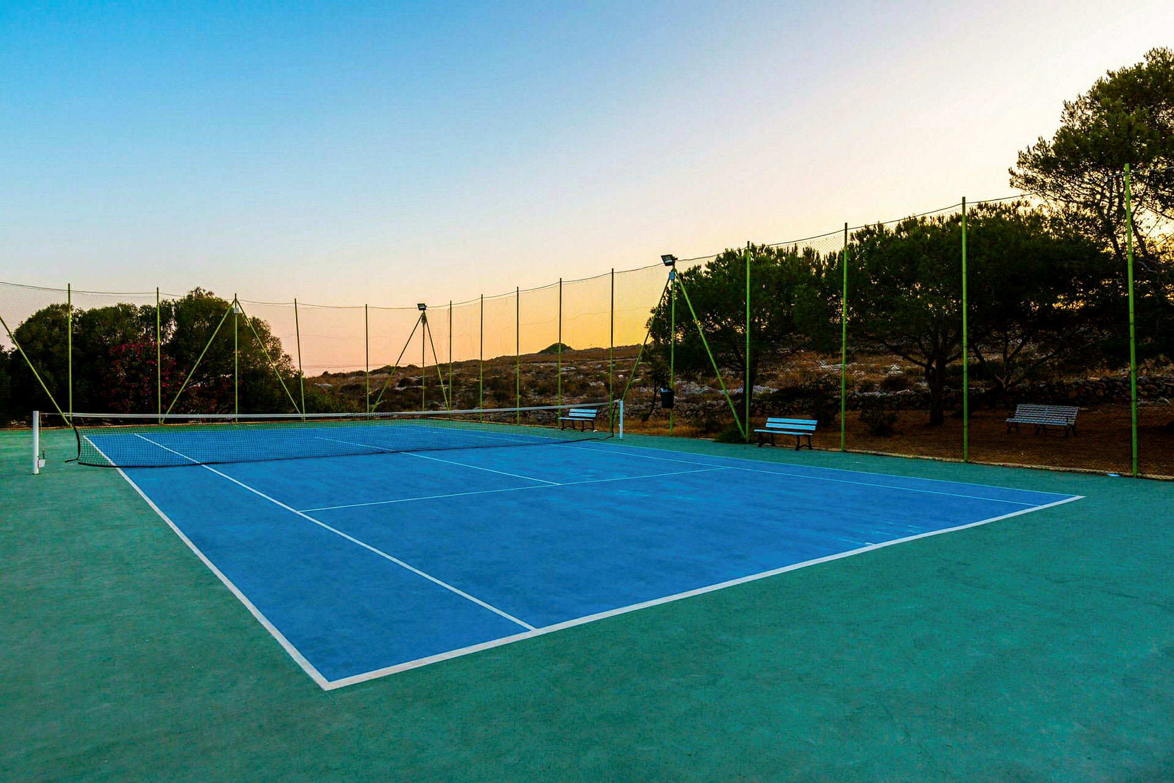 En tennisbana med blå beläggning omgivet av grönt nät och träd. (AI-genererad text)