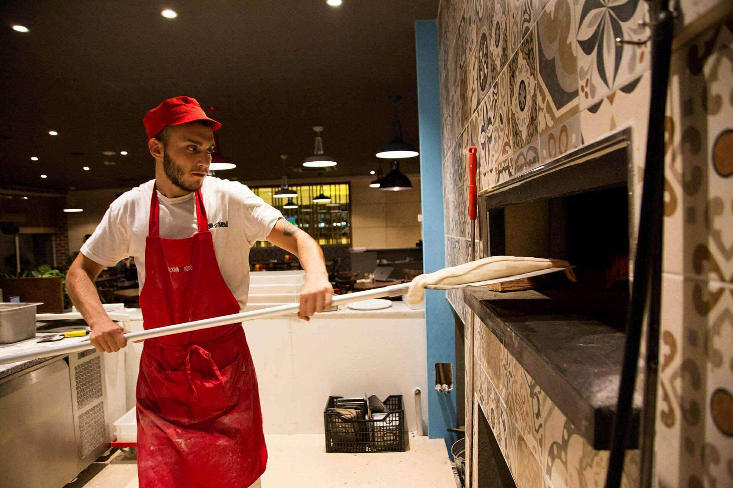 En kock i arbetskläder förbereder en pizza och placerar den i en vedeldad ugn. (AI-genererad text)