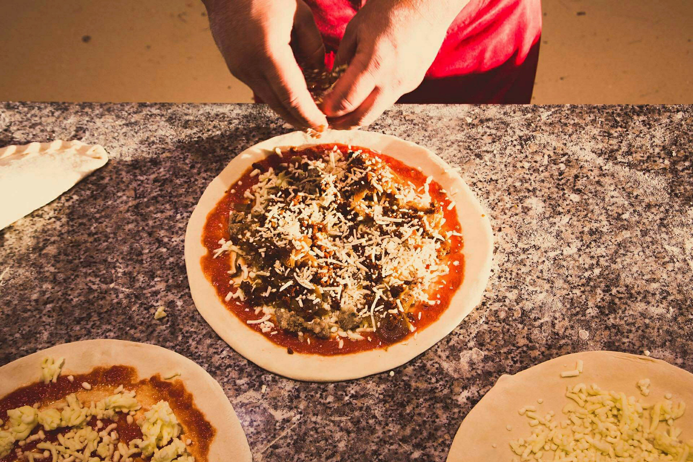 En person förbereder en pizza med toppings på en marmorbänk. (AI-genererad text)