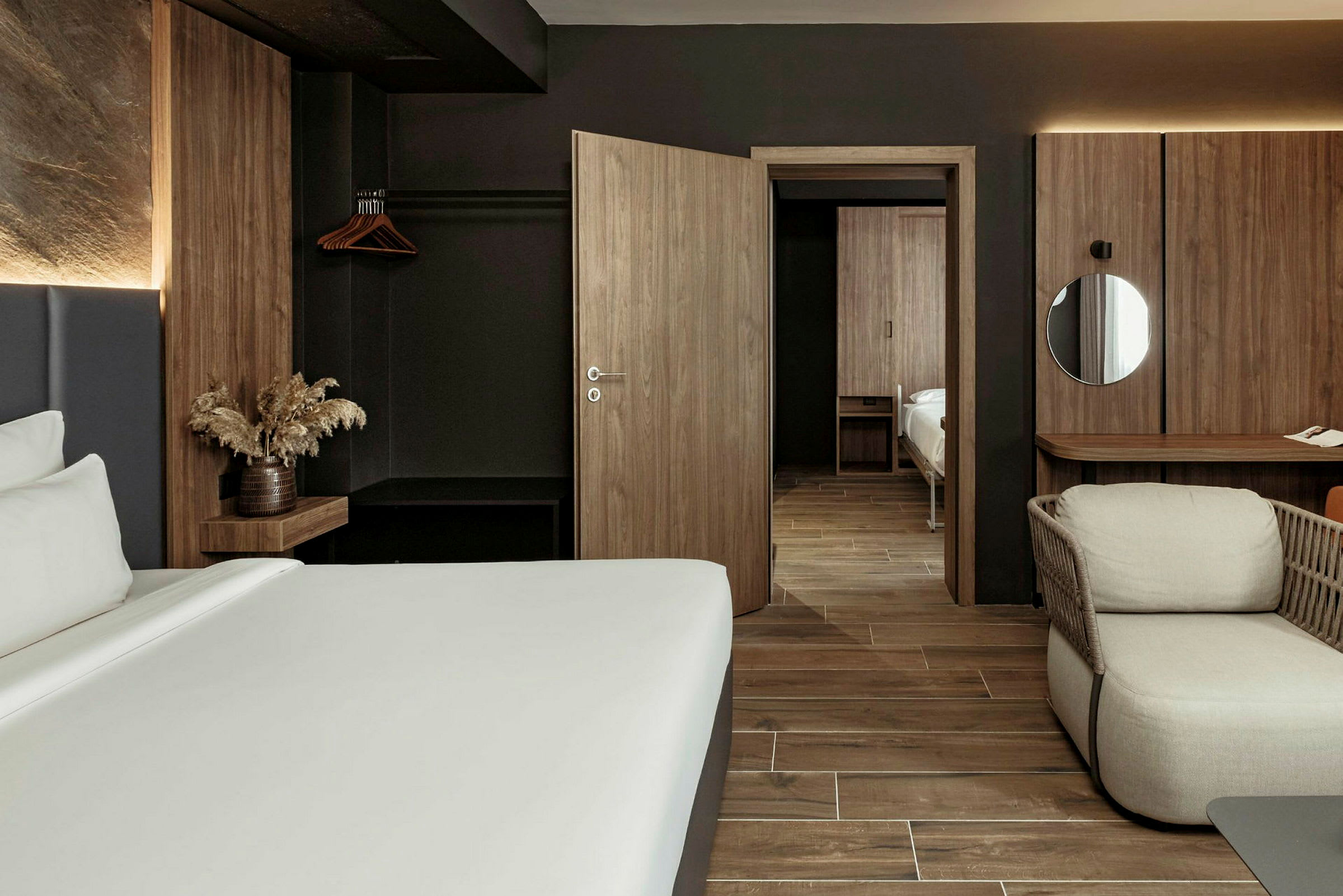 Ett modernt hotellrum med mörka trämöbler och minimalistisk design. En säng, en fåtölj och ett skrivbord syns i rummet. (AI-genererad text)