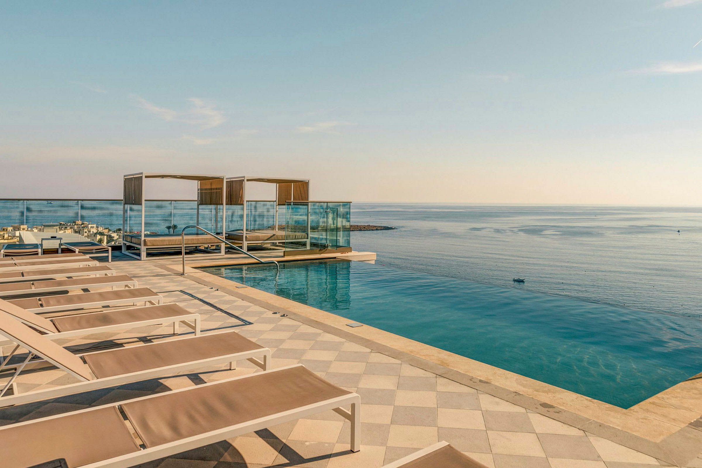 En infinitypool vid havet med solstolar och skuggande cabanas, samt ett räcke mot vattnet. (AI-genererad text)