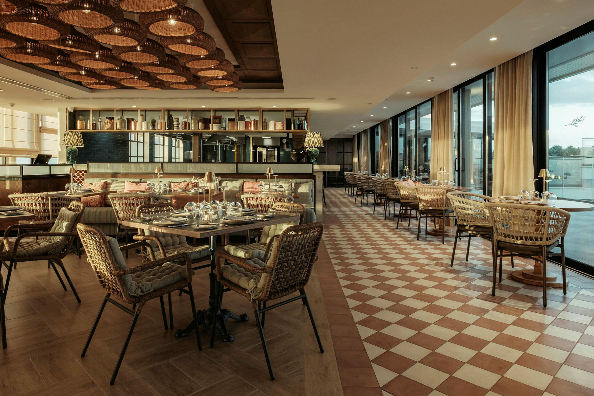 En smakfullt inredd restaurang med bord och rottingstolar. Golvet är rutmönstrat och taket dekorerat med flätade lampor. (AI-genererad text)