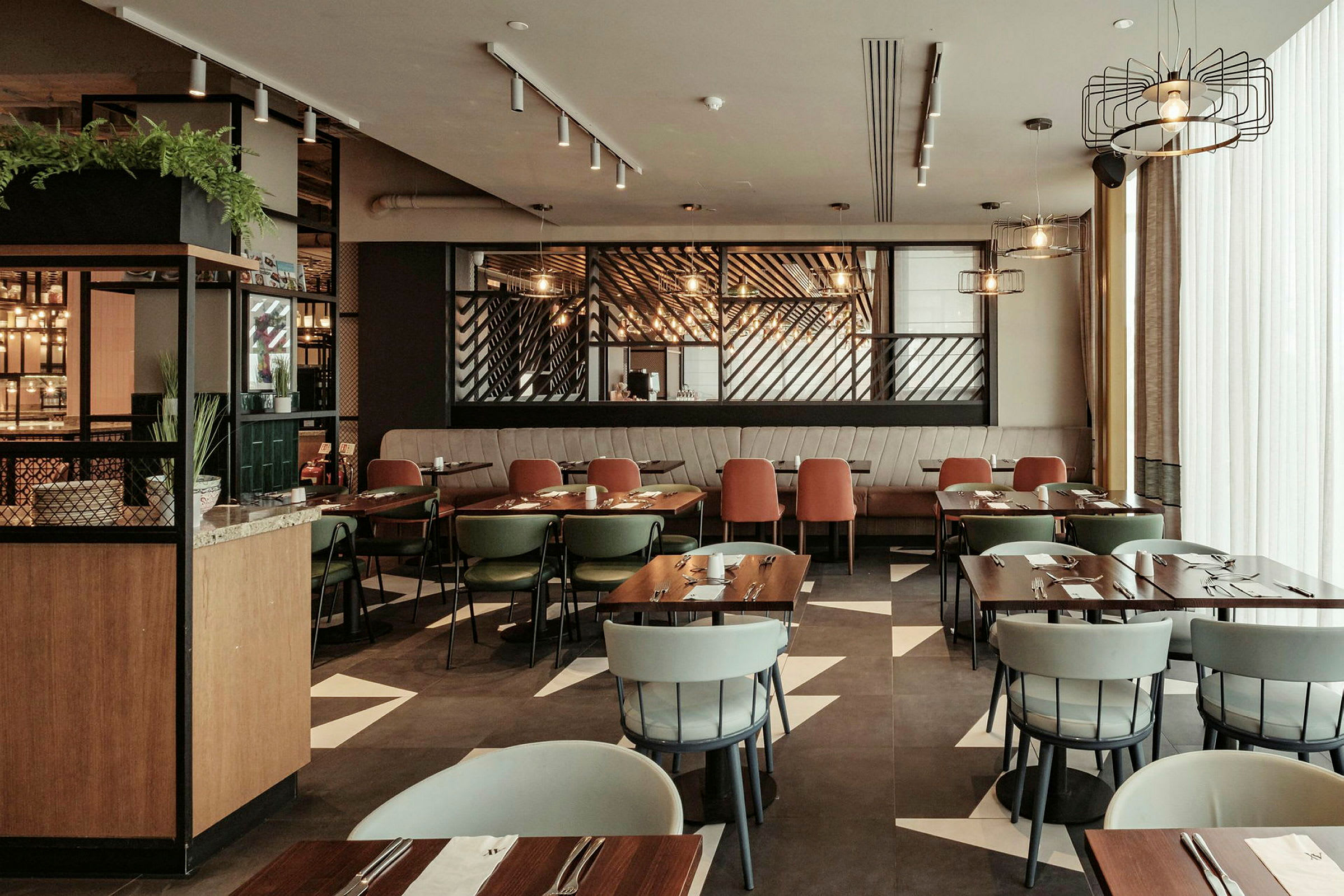 Ett modernt inrett restaurangområde med flera bord och stolar, ljussättning och dekorativa element. (AI-genererad text)
