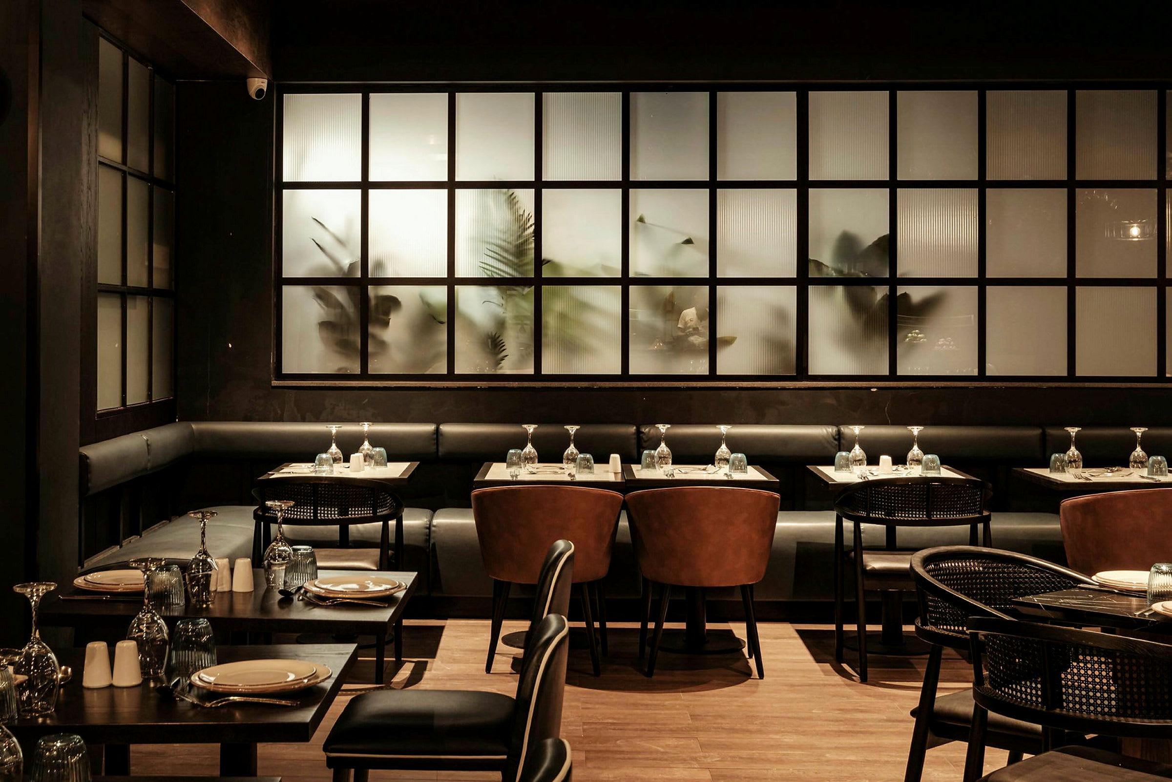 En elegant restaurang med mörk inredning, dukade bord och stolar framför frostade glasfönster. (AI-genererad text)