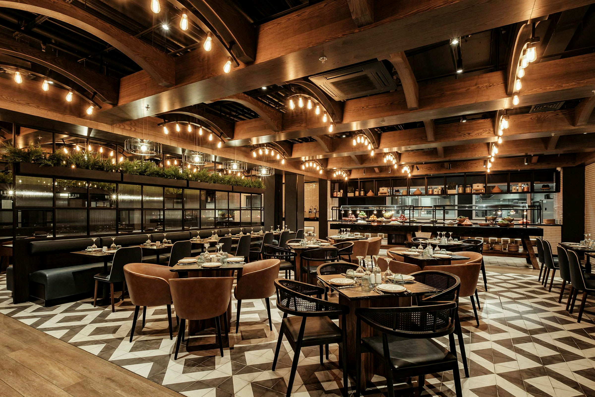 En restaurang med moderna möbler, bord dukade med glas och bestick, samt en elegant atmosfär med dekorativa ljuskällor och trädetaljer. (AI-genererad text)