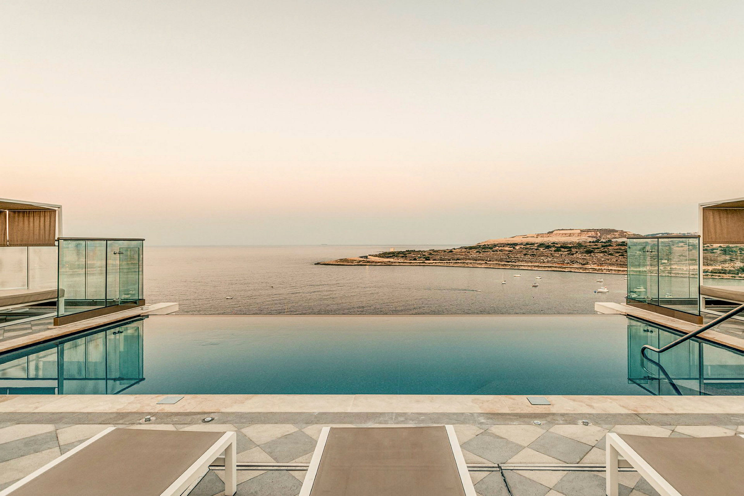 En infinitypool med vy över havet och en kustlinje i horisonten. Stolar står uppställda vid poolens kant. (AI-genererad text)