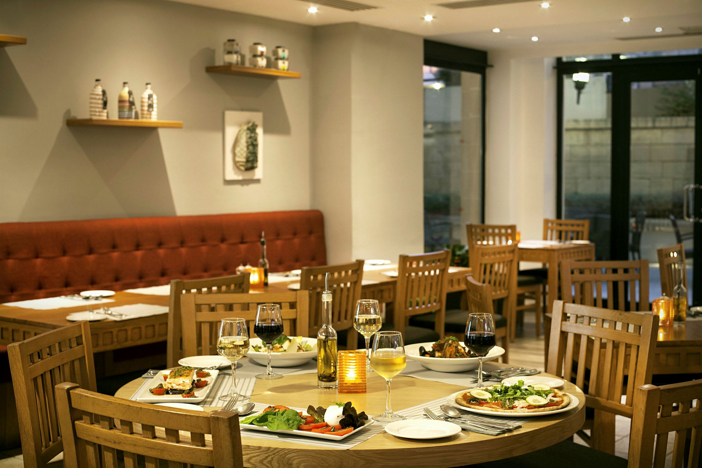 Ett smakfullt inrett restaurangområde med dukade bord och olika rätter. Stolar och bord är av trä, och en bekväm bänksits syns vid väggen. (AI-genererad text)