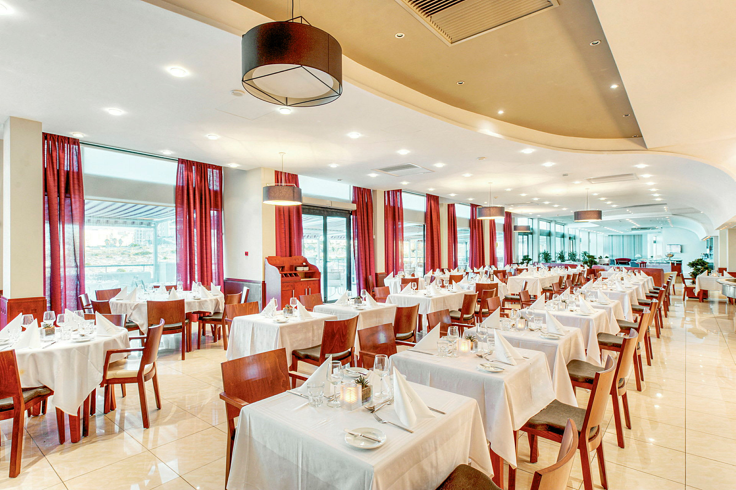 En ljus restaurang med bord klädda i vita dukar och röda gardiner vid fönstren. (AI-genererad text)