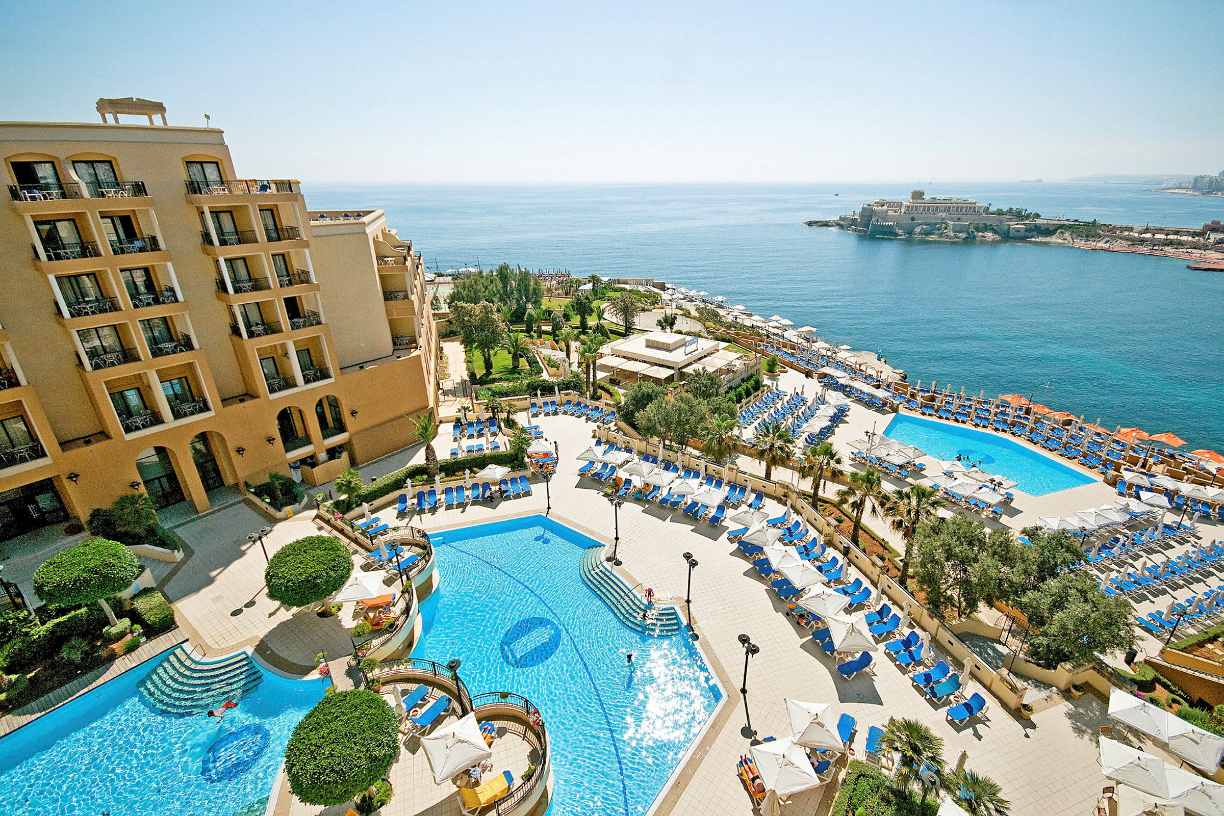En hotellanläggning med pooler, solstolar och parasoller, samt havsutsikt. (AI-genererad text)