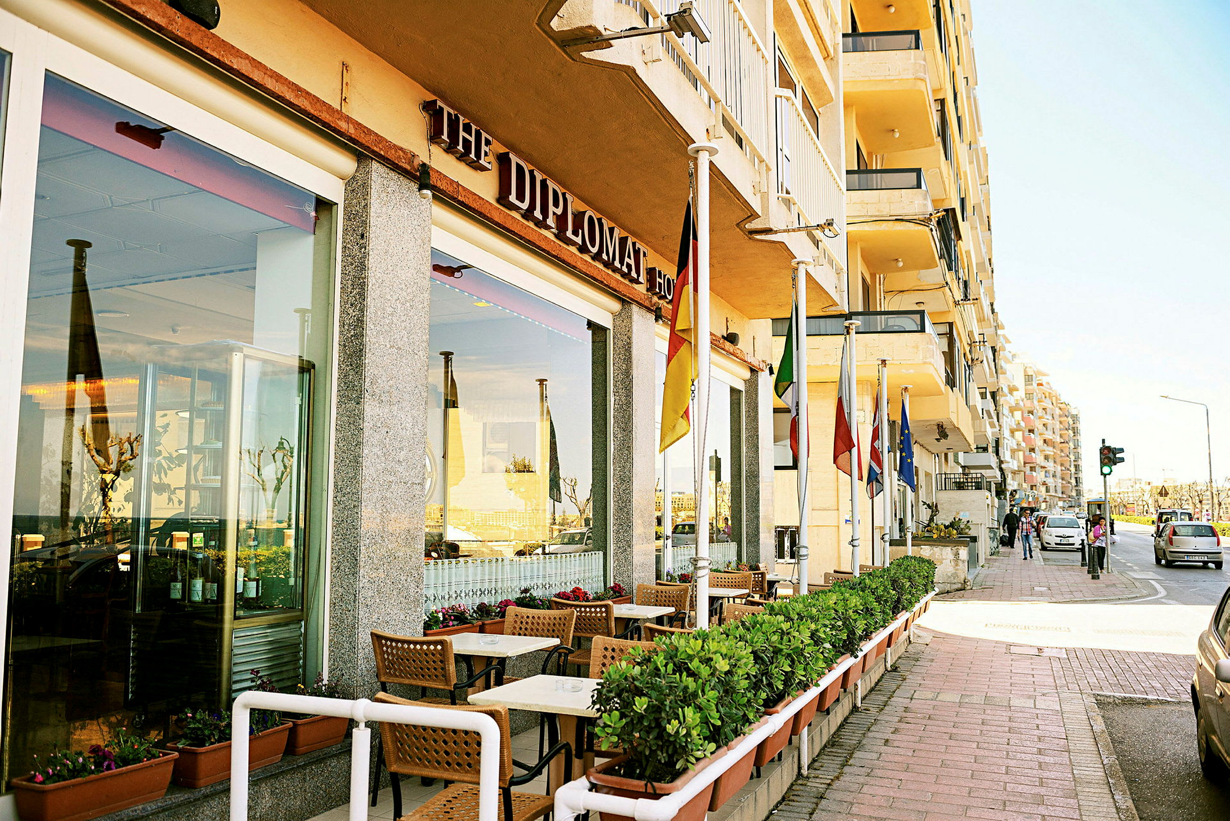 Restaurang med uteservering samt olika flaggor vid entrén utmed en trottoar. (AI-genererad text)
