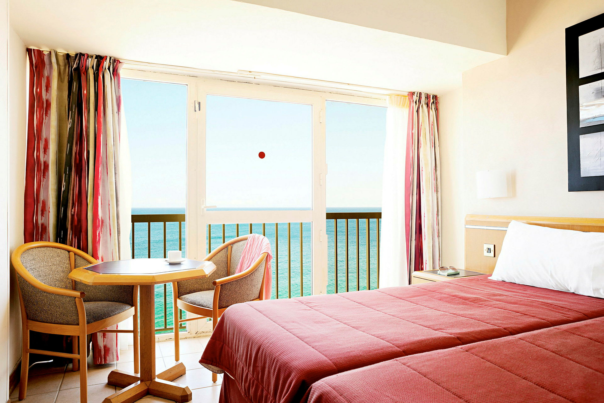 Ett hotellrum med två bäddar, ett litet bord och två stolar, samt en balkong med utsikt över havet. (AI-genererad text)