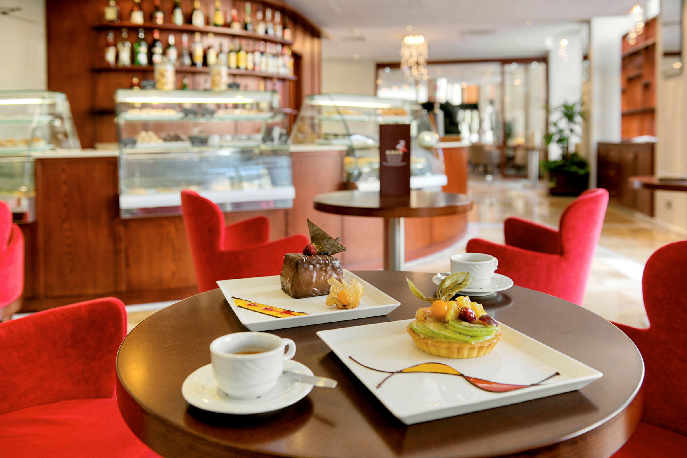 En kaféinteriör med röda stolar, ett bord dukat med kaffe och desserter, och en bakgrund med vistelser och skåp. (AI-genererad text)