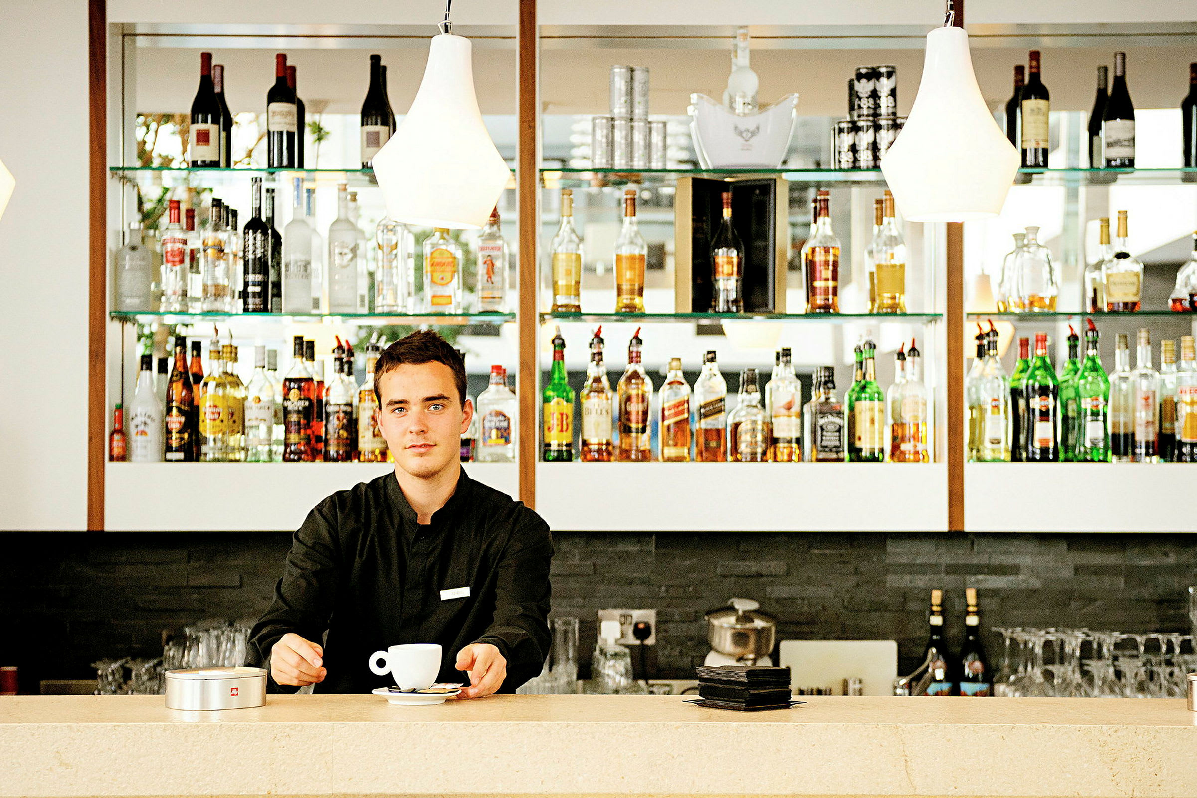 En bartender i en bar med hyllor fyllda med flaskor med alkohol. (AI-genererad text)