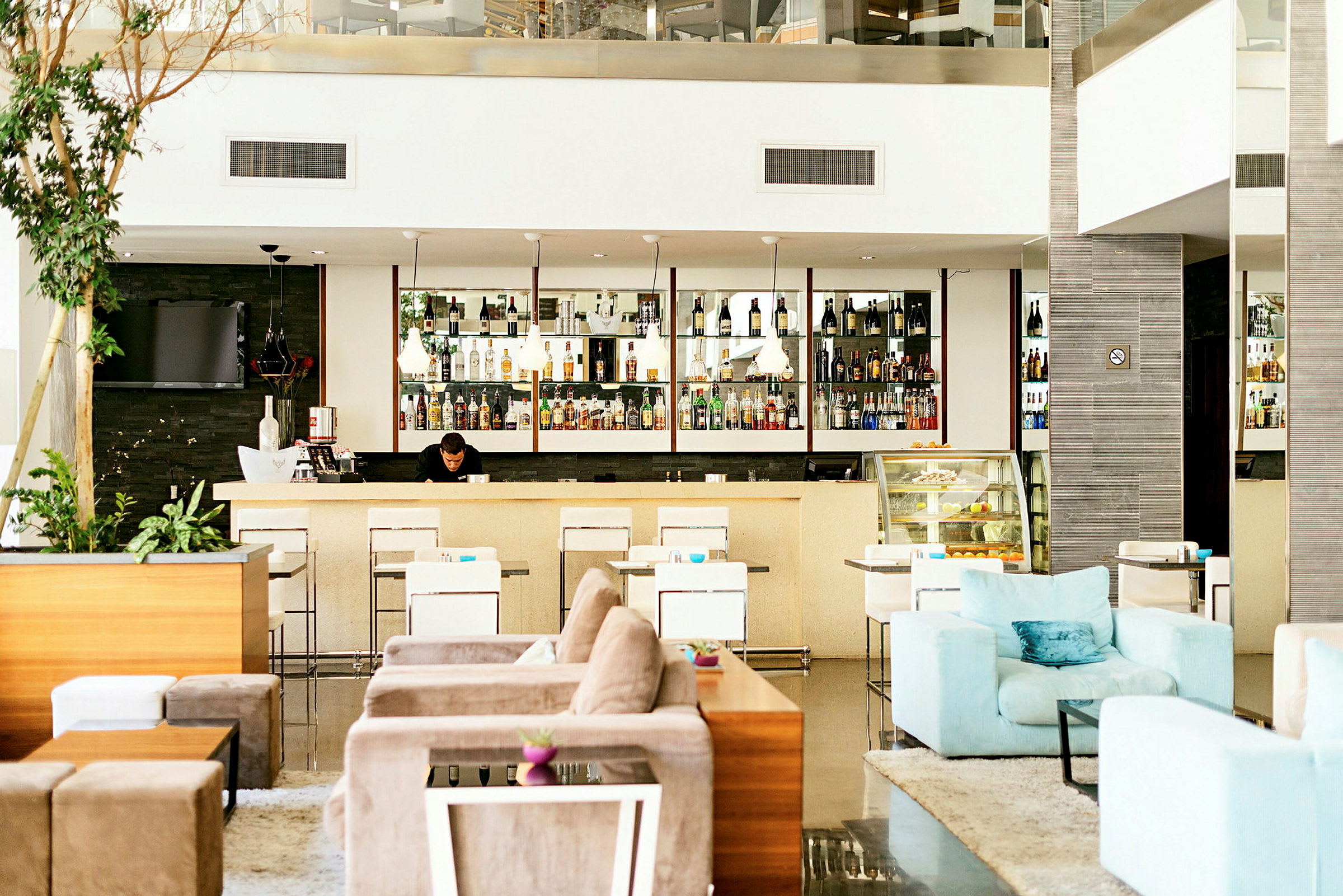 En hotellobby med en väl belyst bar, moderna sittmöbler och en avslappnad atmosfär. (AI-genererad text)