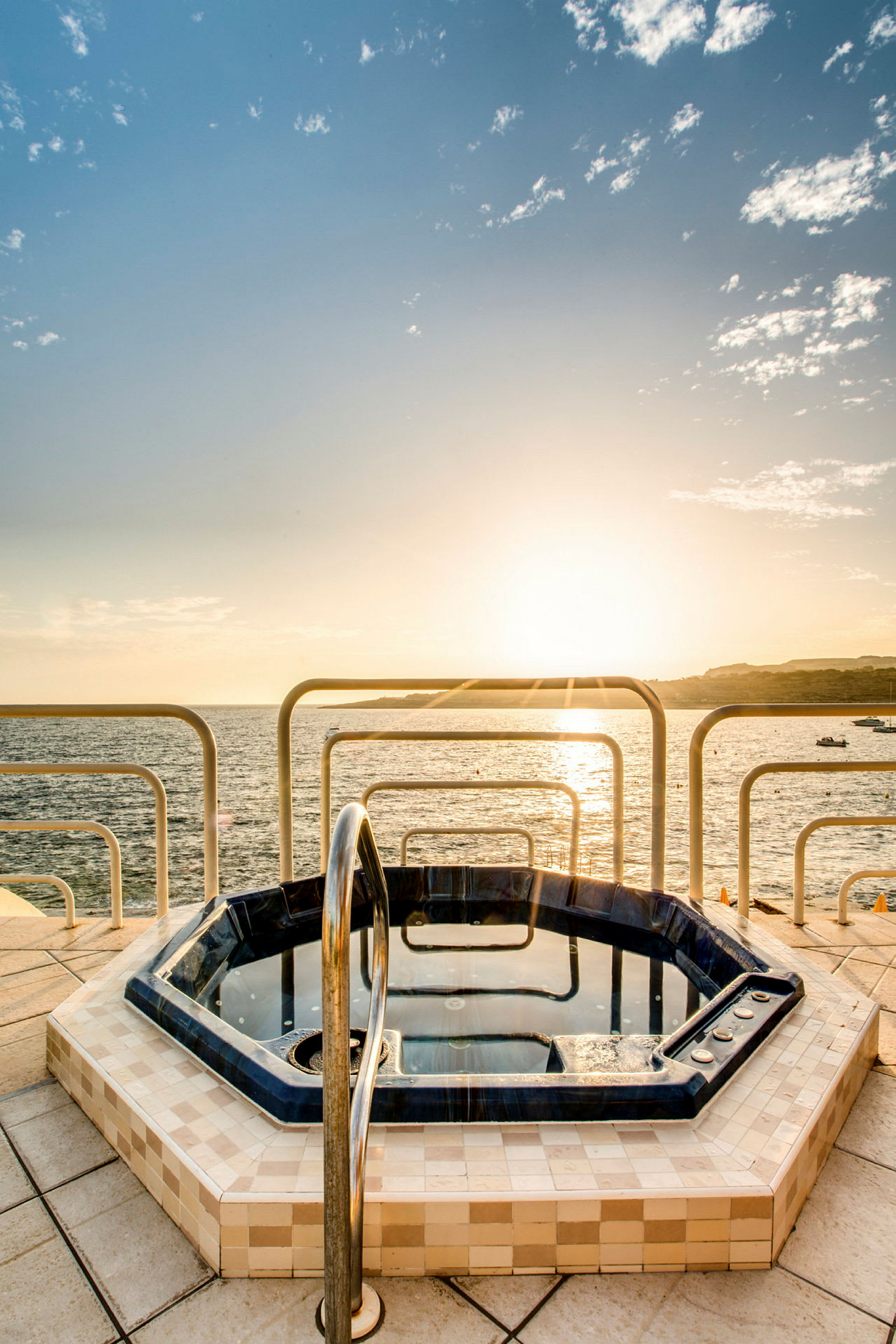 En badtunna på en terrass med utsikt över havet och en solnedgång. (AI-genererad text)