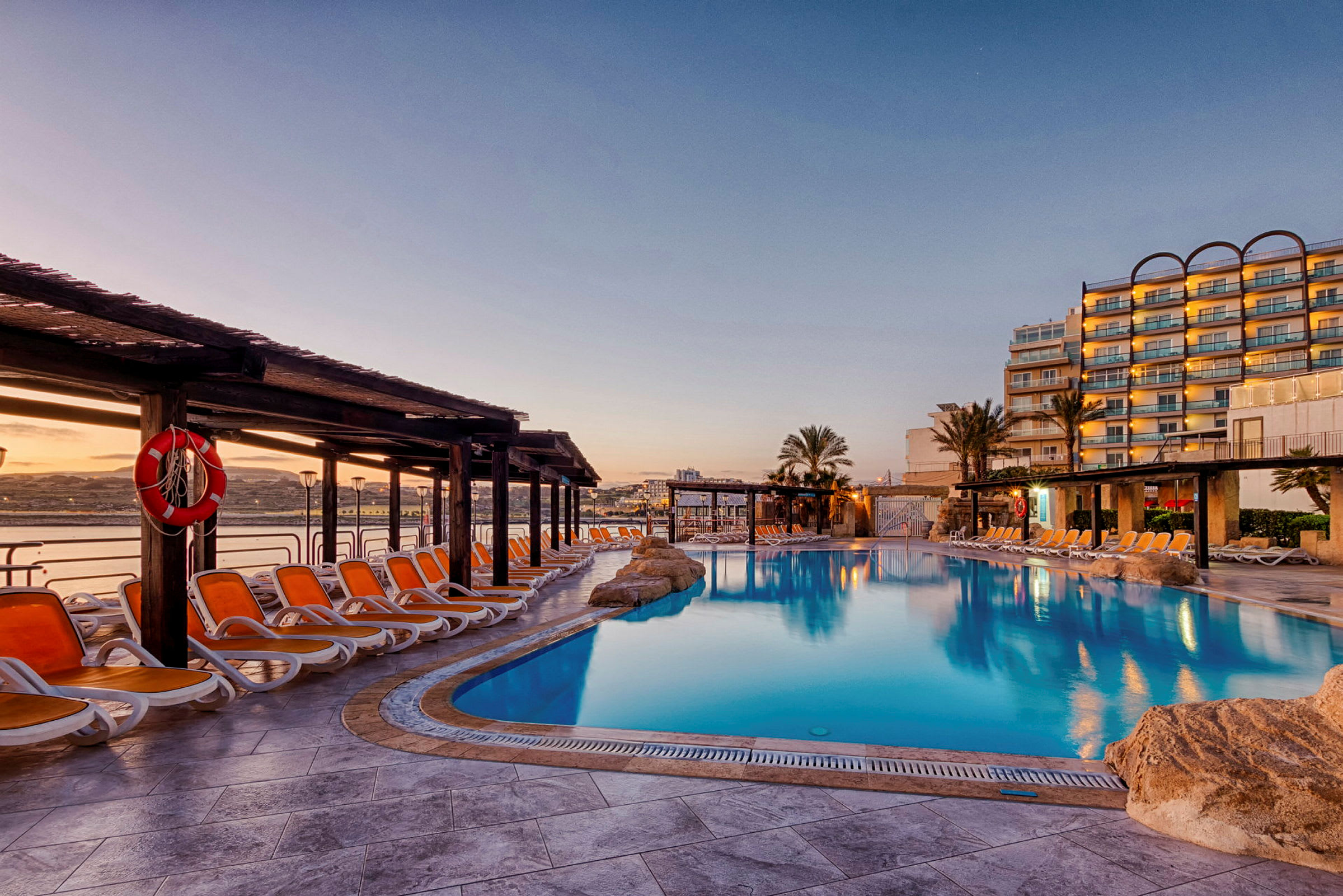 Bild av ett hotellpoolområde med solstolar, parasoller och en stor swimmingpool vid solnedgången. (AI-genererad text)