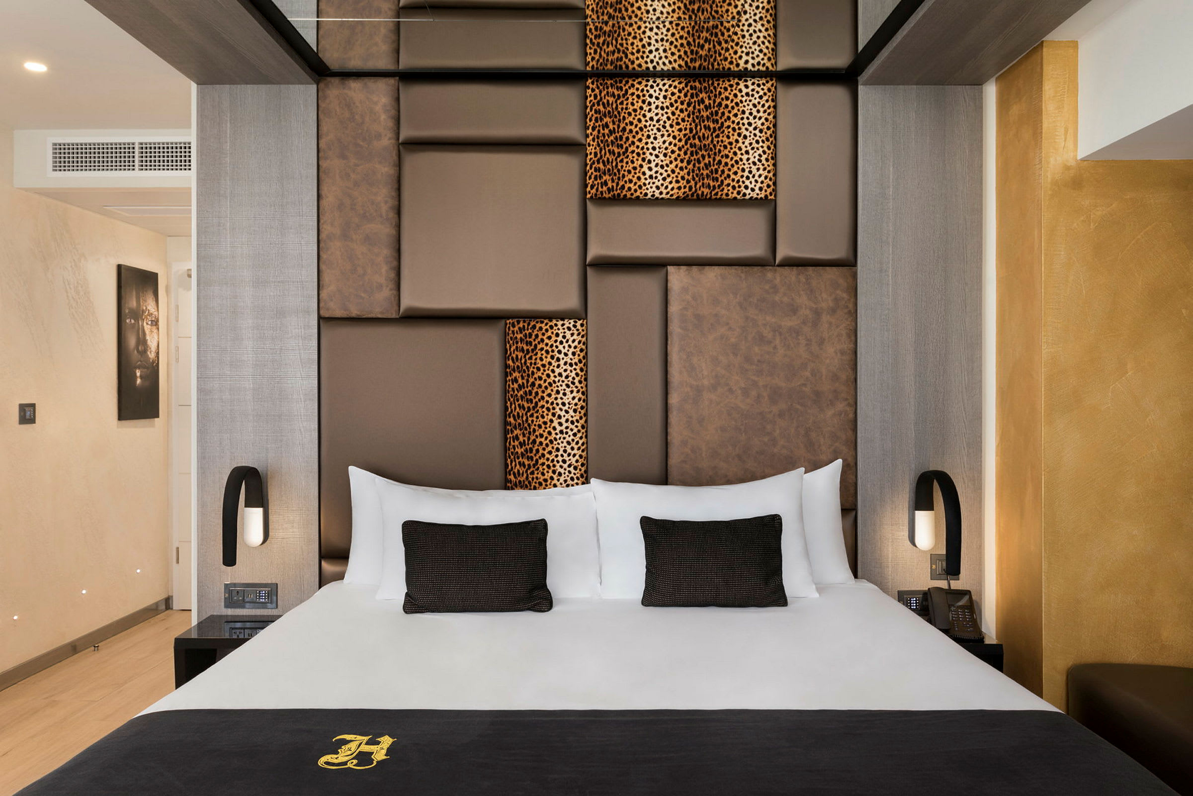 En elegant hotellrum med en stor säng, med bruna och mönstrade paneler på väggen bakom. Rummet är modernt inrett med varma färger. (AI-genererad text)