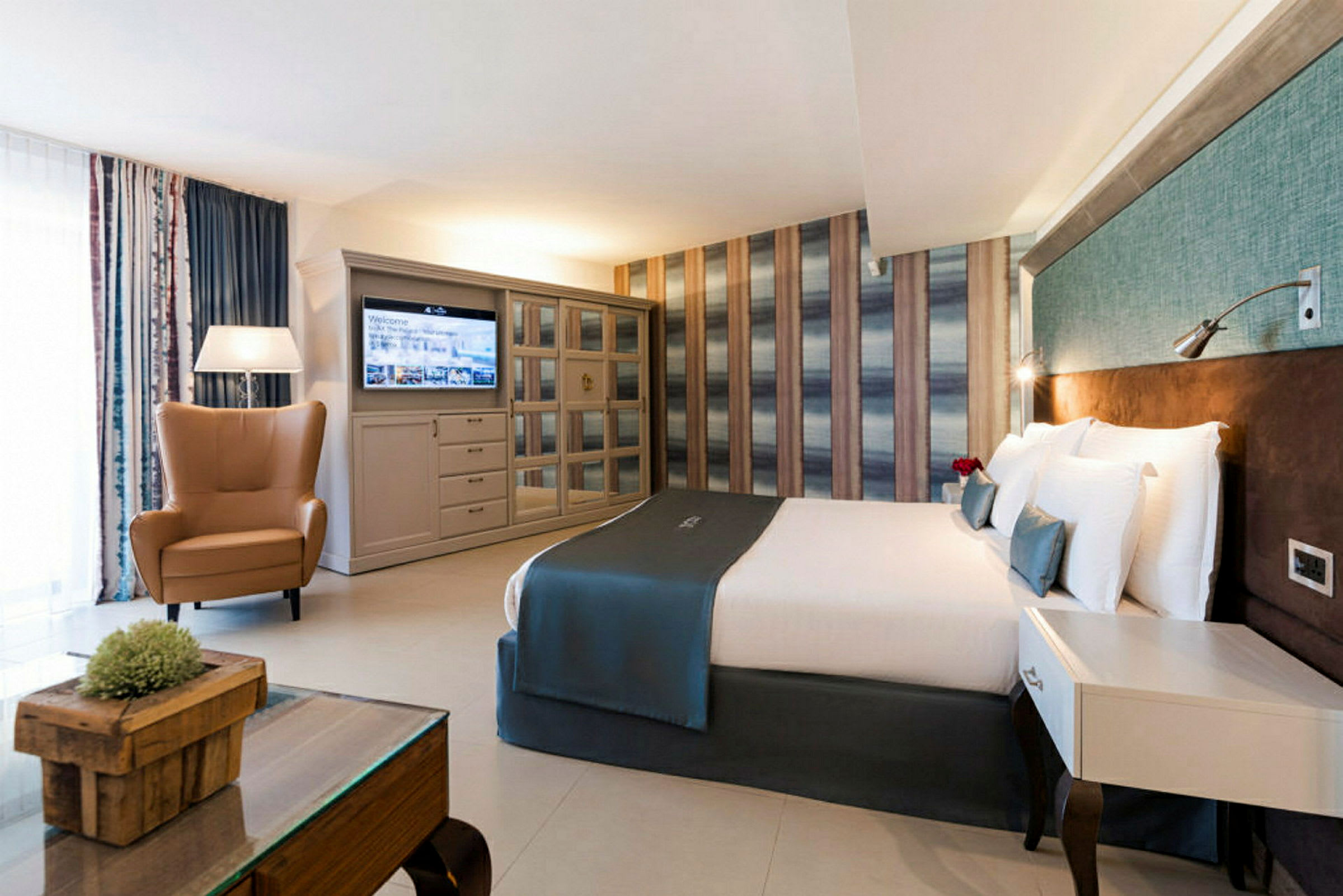 Ett hotellrum med en dubbelsäng, en fåtölj, ett bord och en tv på väggen. (AI-genererad text)