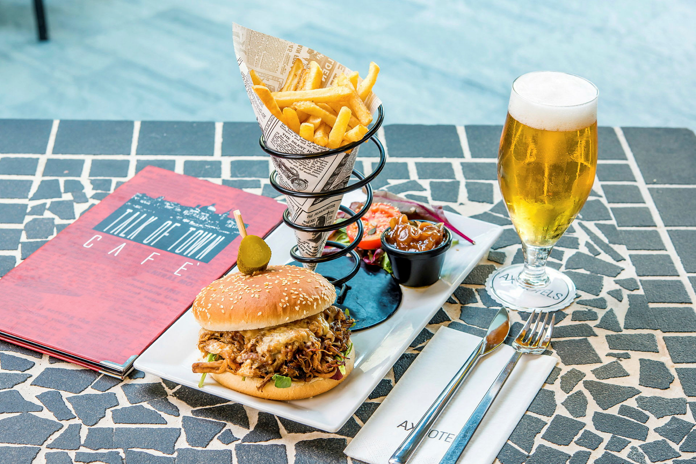 En tallrik med en hamburgare, pommes frites, sallad, sås samt ett glas öl på ett bord. (AI-genererad text)