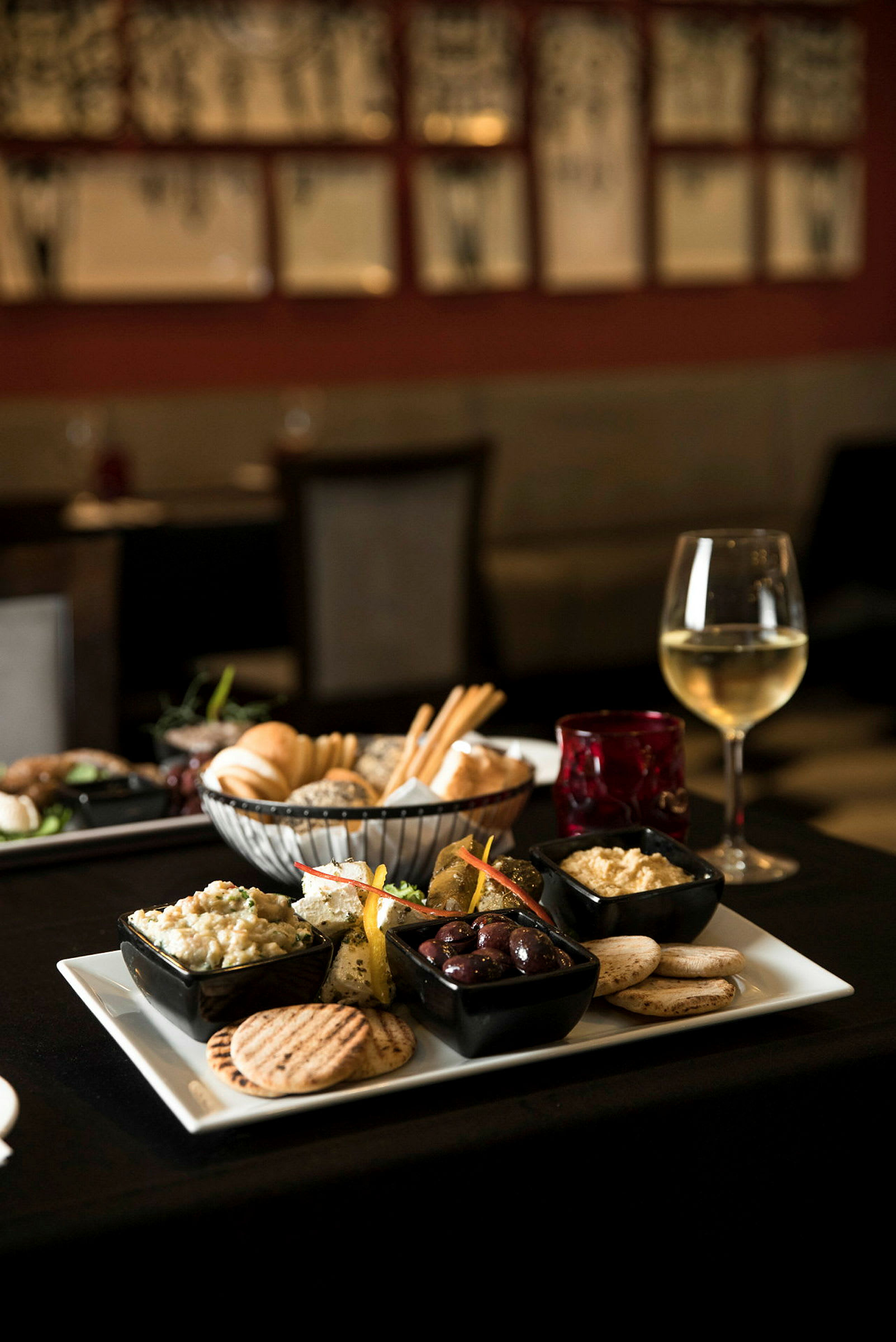 En bricka med olika smårätter, inklusive oliver, hummus och bröd, serveras tillsammans med ett glas vitt vin. (AI-genererad text)
