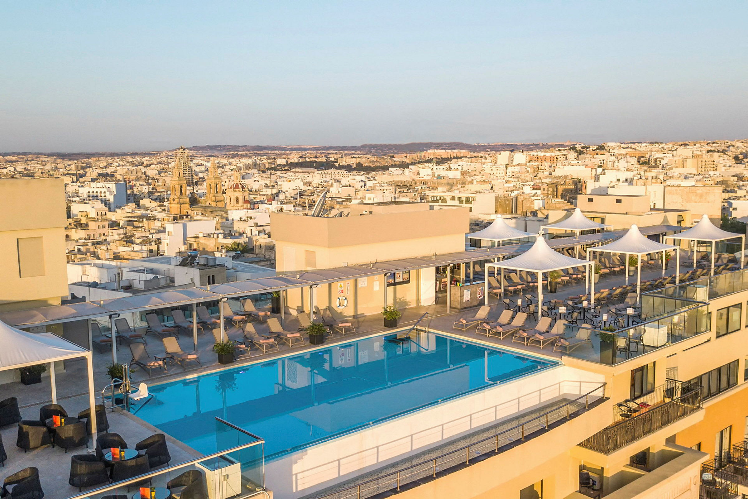 Bild av en takterrass med en pool, solstolar och utsikt över en stad i bakgrunden. (AI-genererad text)