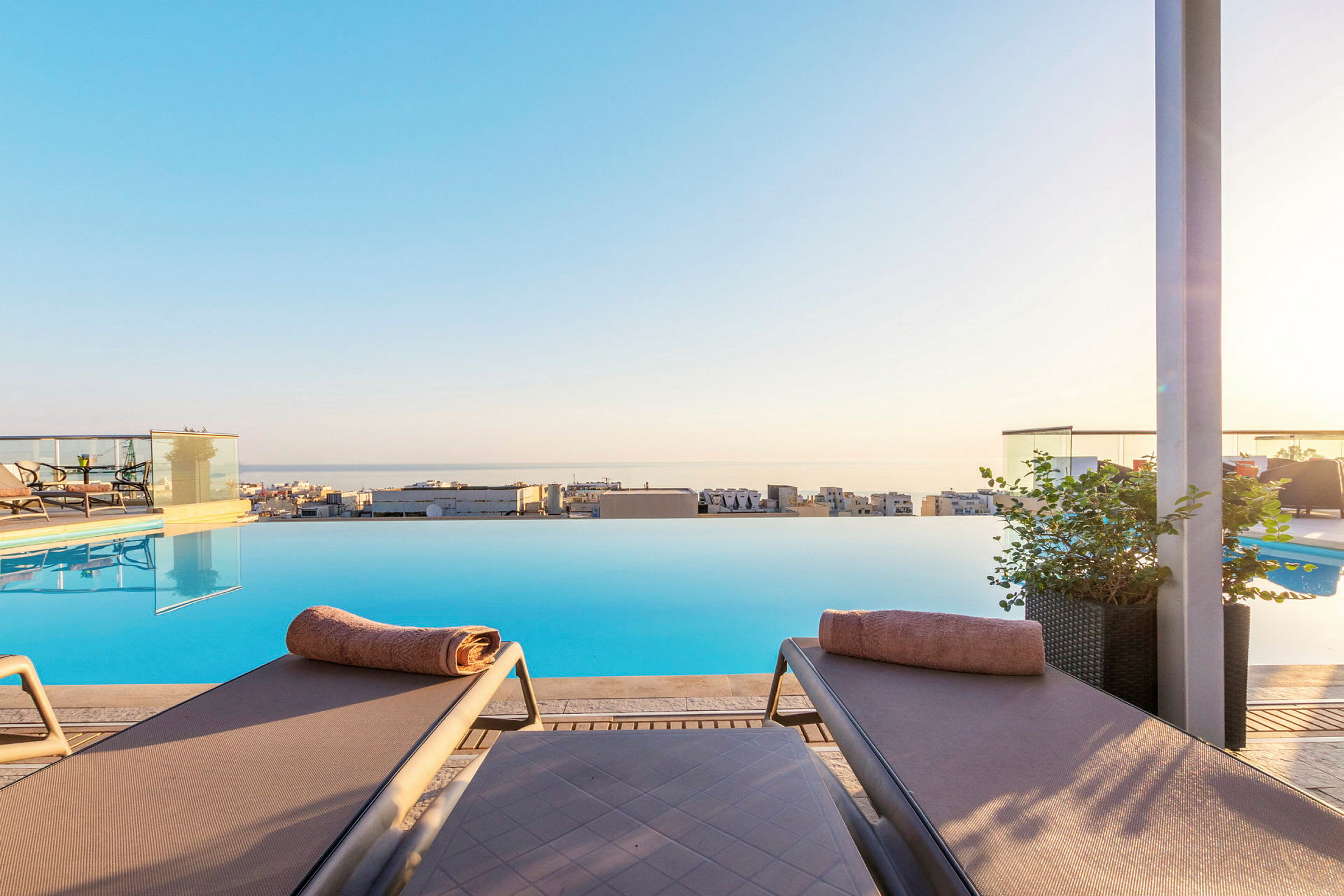Två solstolar med handdukar vid en infinitypool med utsikt över staden och havet. (AI-genererad text)