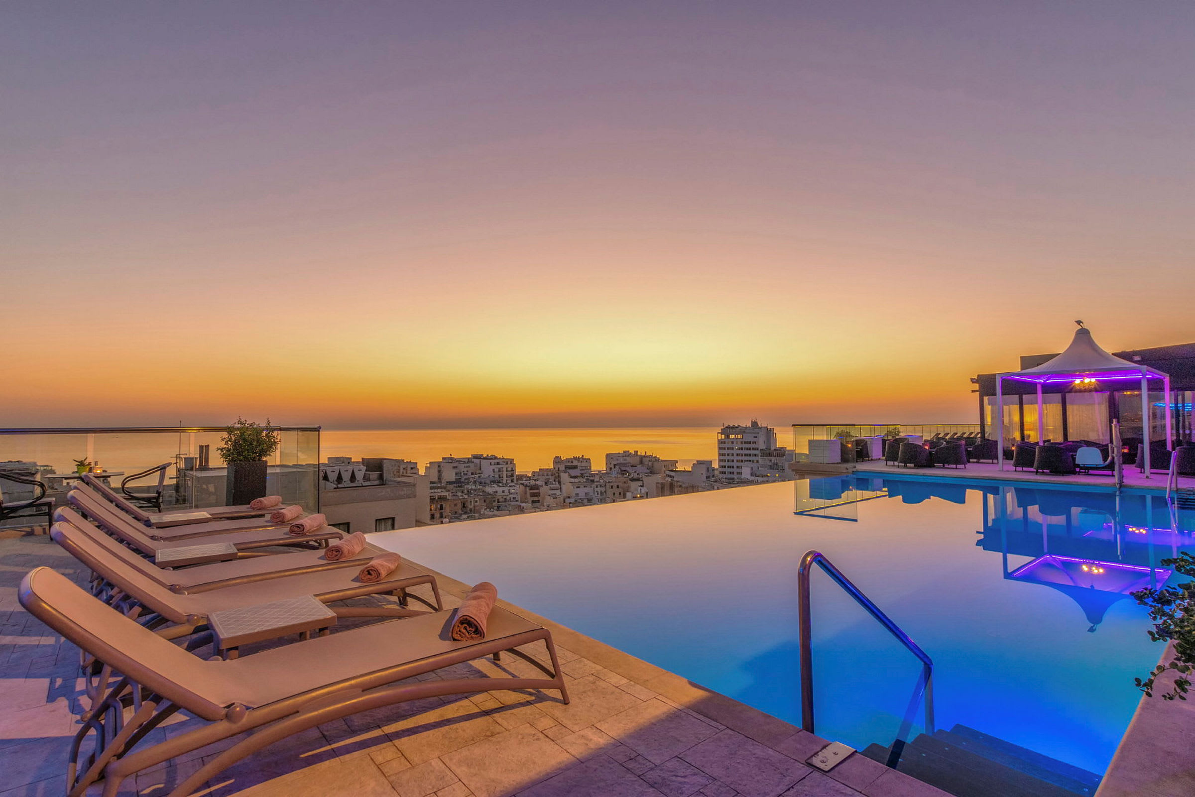 En infinitypool vid solnedgång, med vilstolar och en paviljong i bakgrunden. (AI-genererad text)