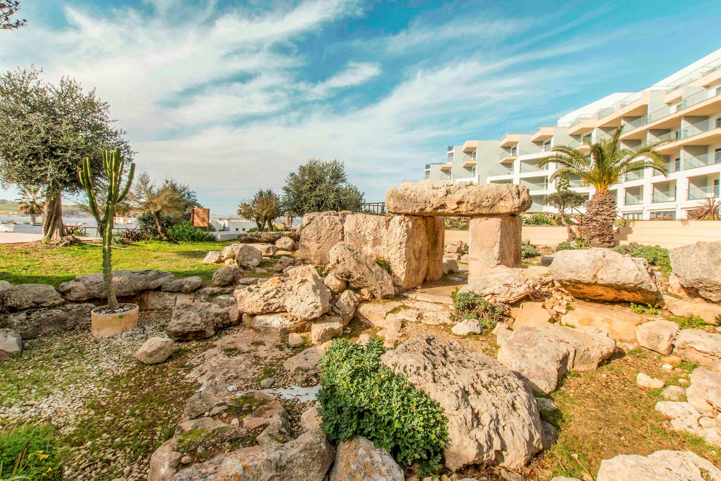 Bild av en äldre stenstruktur i en trädgård nära ett modernt bostadshus. (AI-genererad text)