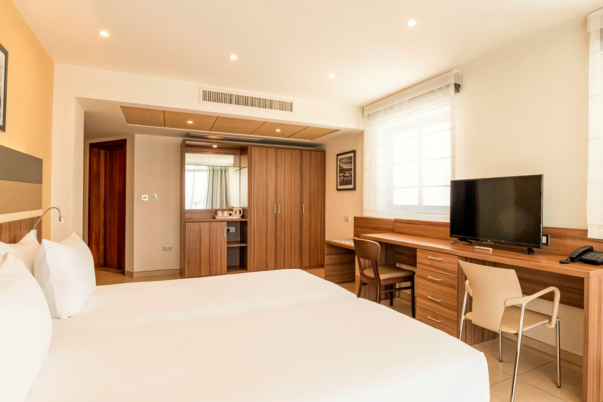 Ett modernt hotellrum med dubbelsäng, träinredning, skrivbord och TV. (AI-genererad text)