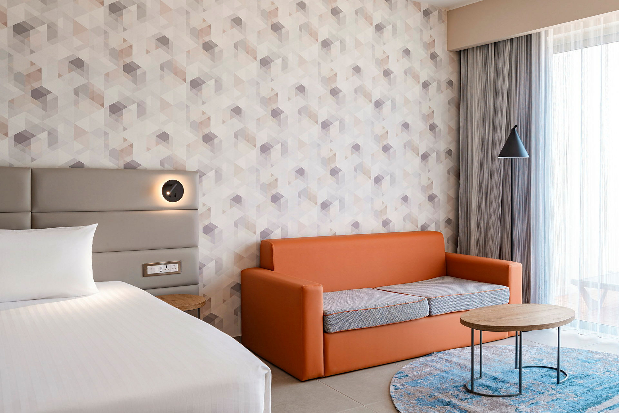 En hotellruminredning med en säng, en orange soffa och ett runt soffbord. (AI-genererad text)