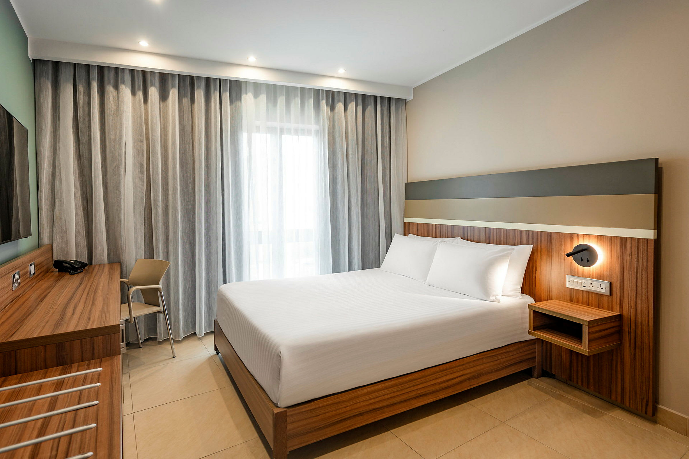 Interiör av ett hotellrum med en stor, snyggt bäddad säng och en skrivbordsyta. (AI-genererad text)