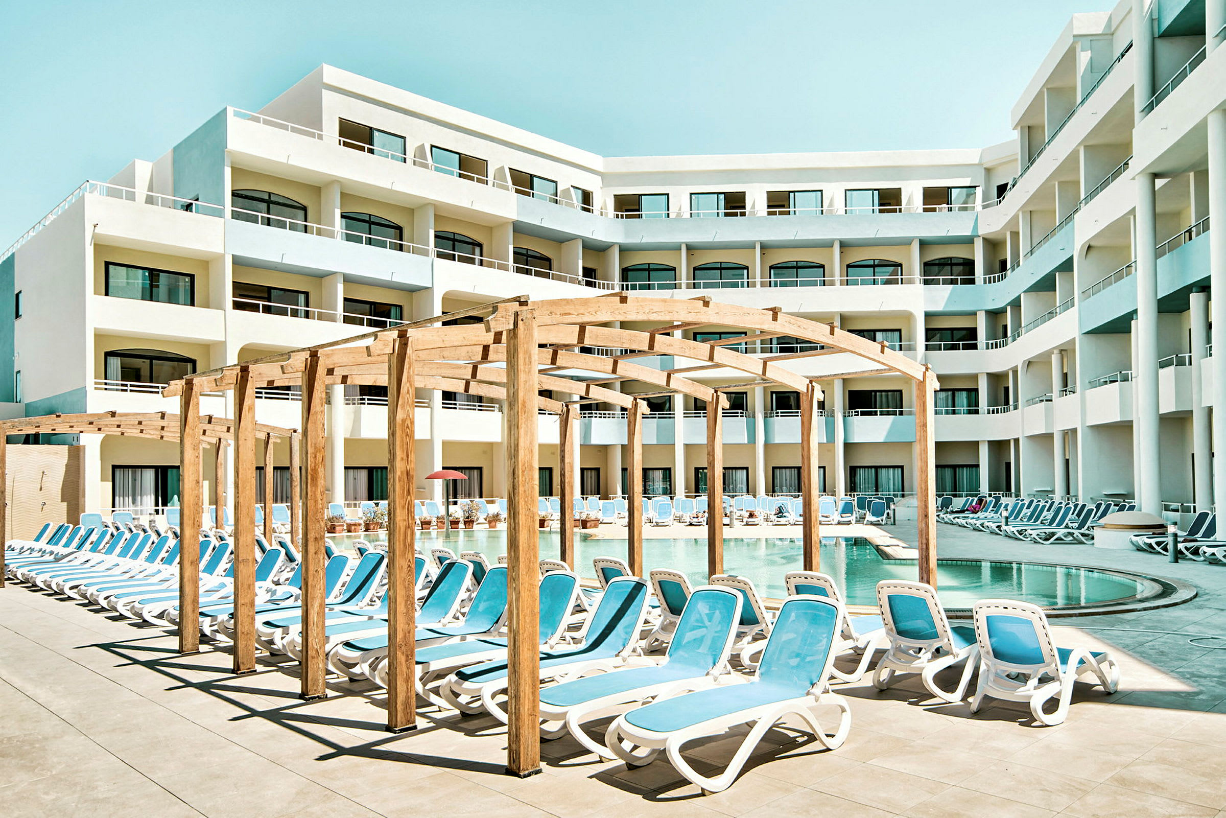 Poolområde vid hotell med solstolar och skuggande pergola. (AI-genererad text)