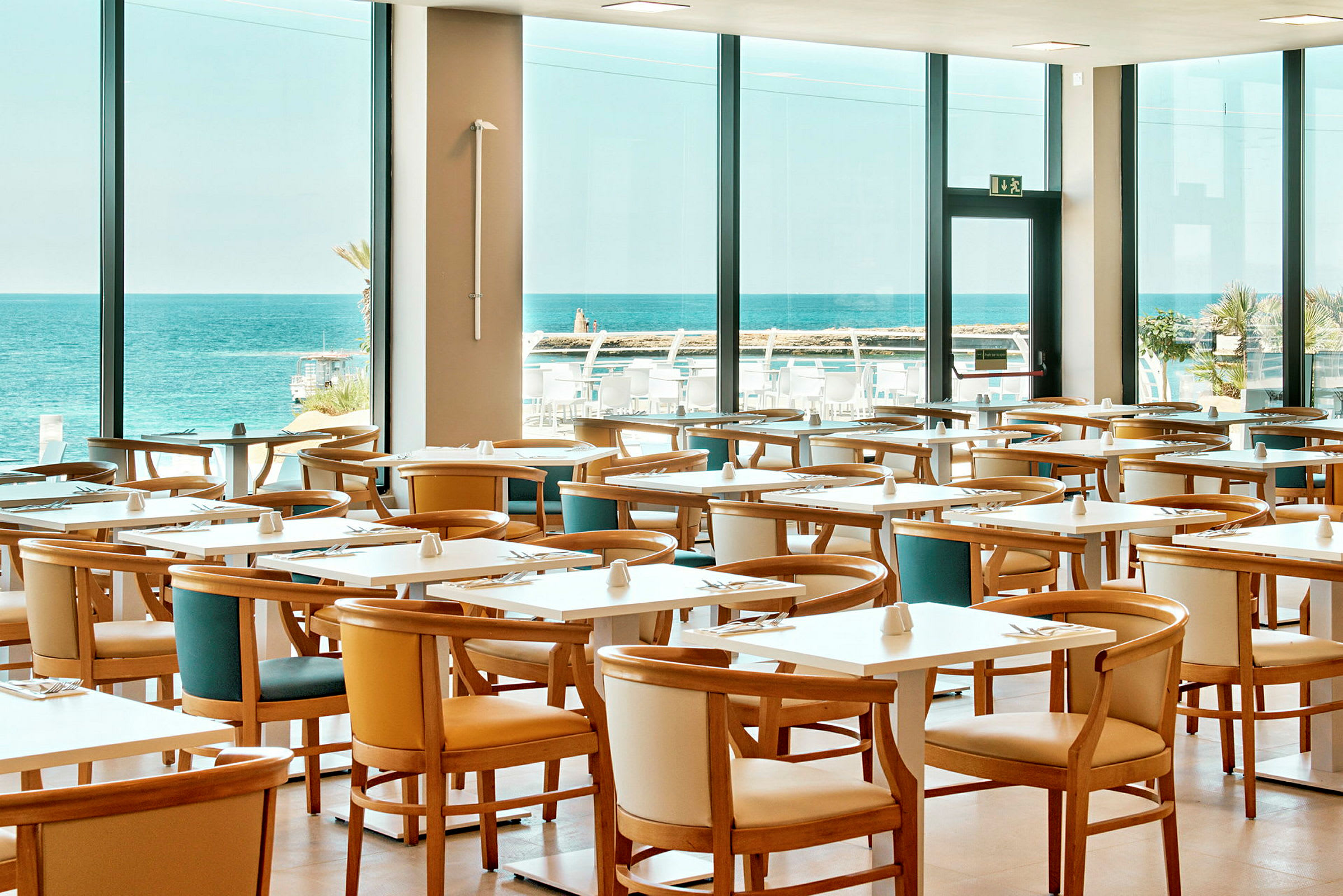 Restaurang med flera bord och stolar, stor fönstervy mot havet. (AI-genererad text)