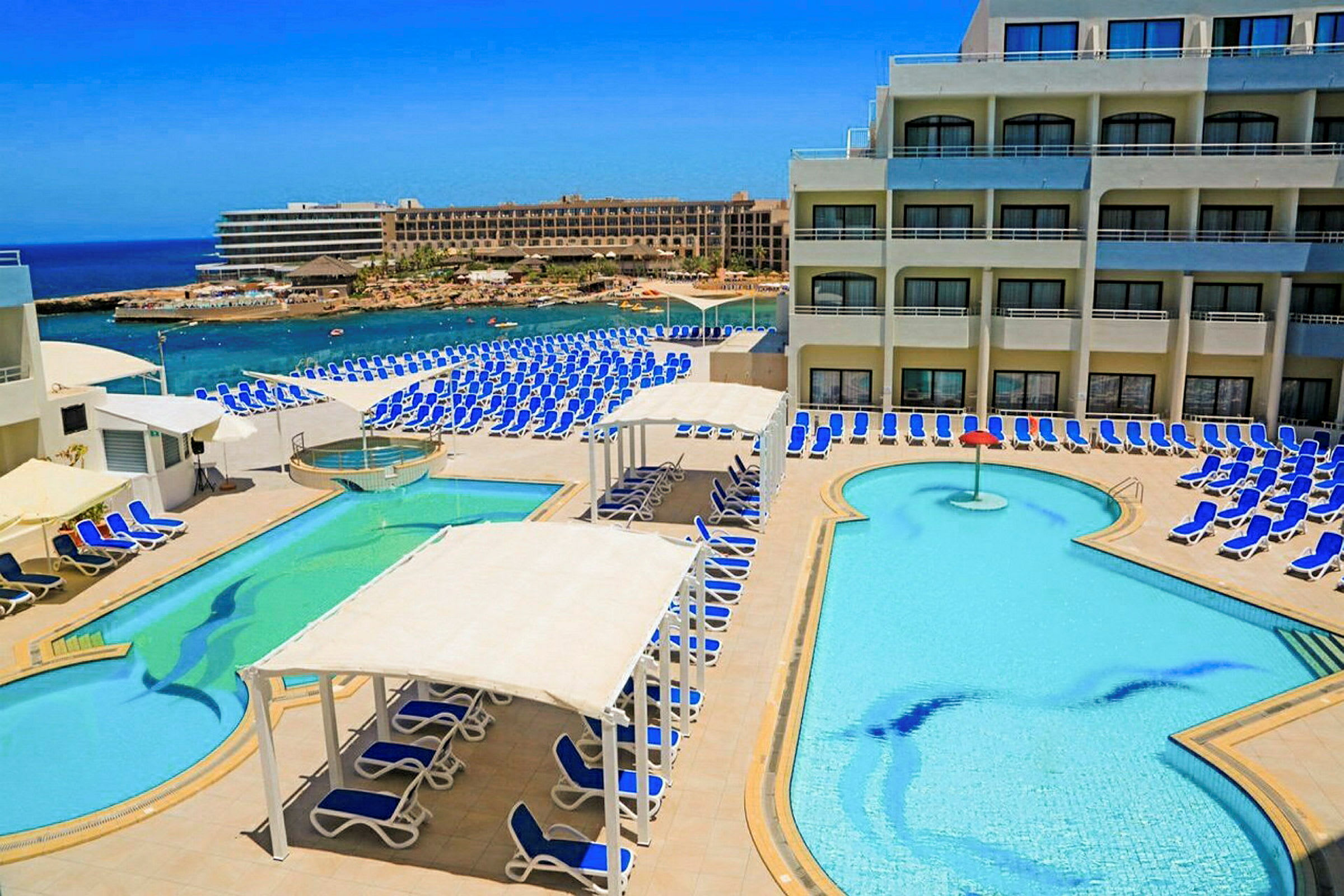 En hotellpool med solstolar och havsutsikt. (AI-genererad text)