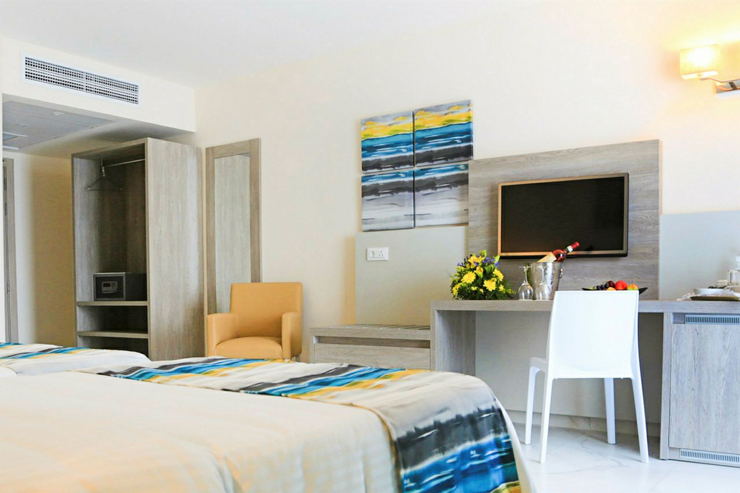 Ett modernt hotellrum med en dubbelsäng, bord och stolar samt en väggmonterad TV. (AI-genererad text)