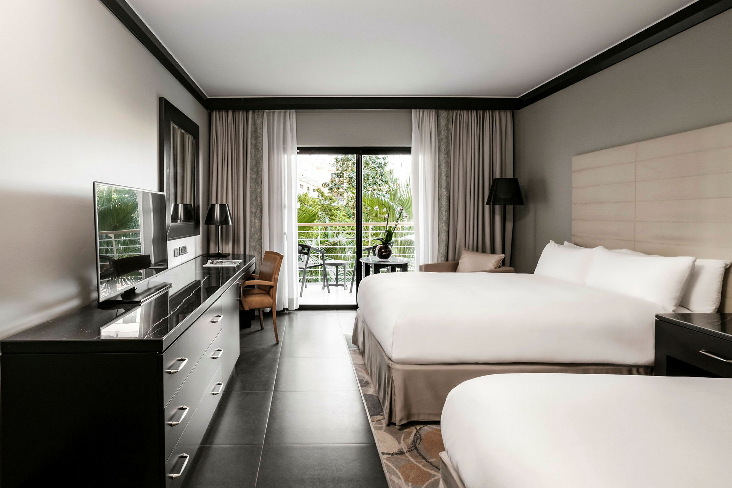 Hotellrum med två sängar, skrivbord, TV och glasdörr som leder ut till en balkong. (AI-genererad text)