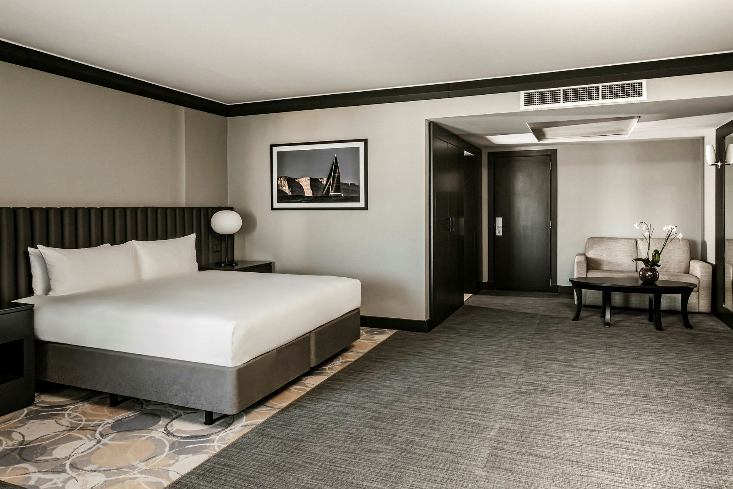 Ett hotellrum med en stor säng, bord och sittgrupp. Väggarna är ljusgrå och inredningen modern. (AI-genererad text)
