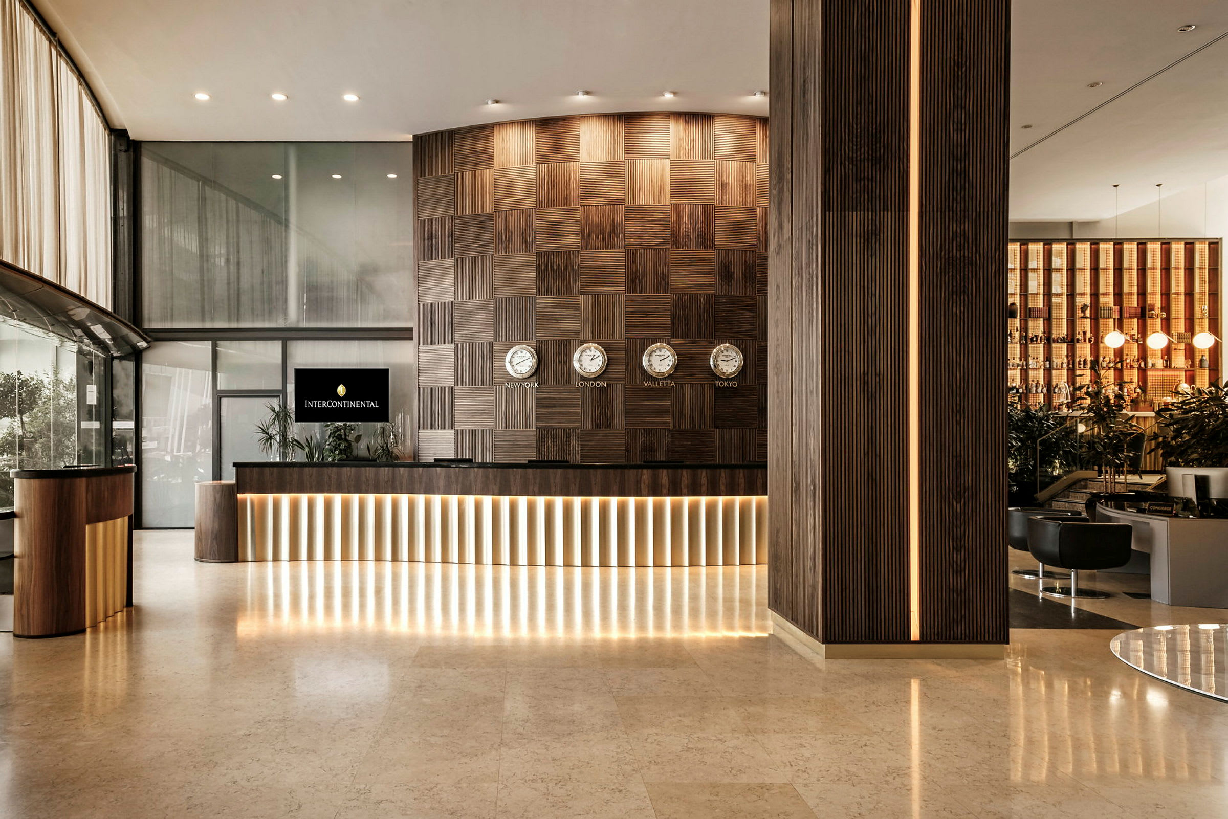 Receptionen på ett hotell med en modern design, mörka träpaneler och flera klockor som visar olika tidszoner. (AI-genererad text)