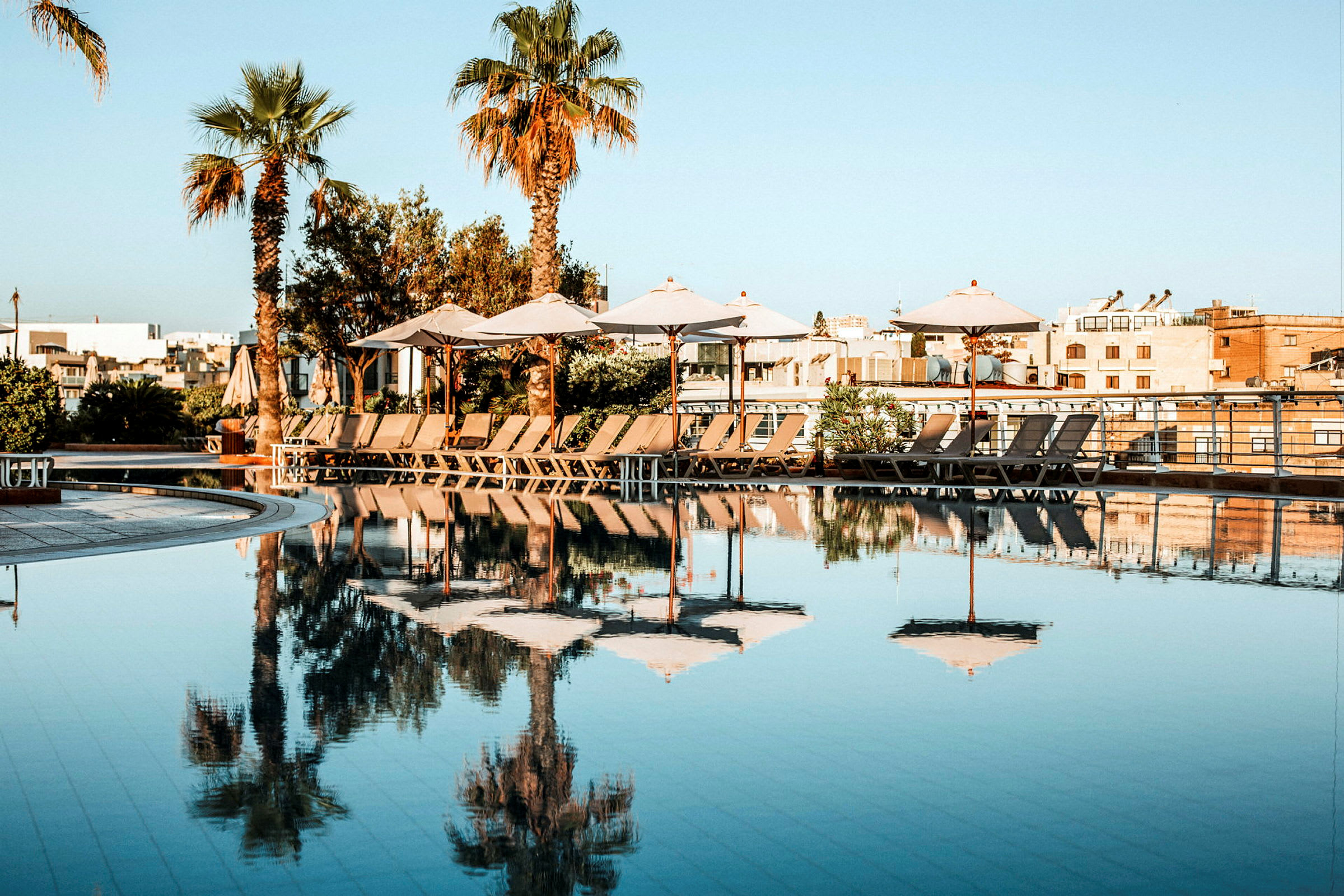 En pool med parasoller och solstolar på en solig dag. (AI-genererad text)