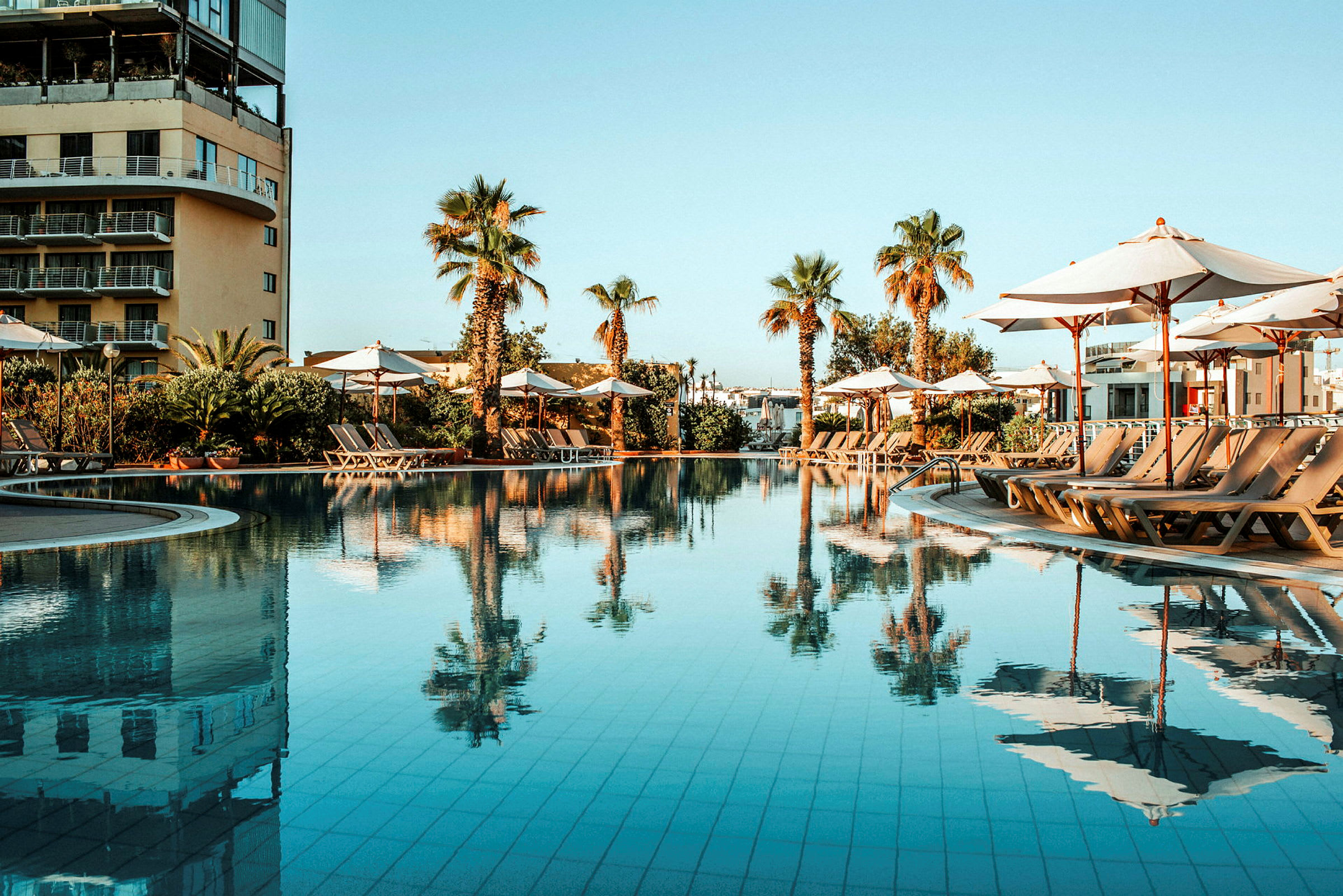 En pool med solstolar och parasoller omgiven av palmträd. (AI-genererad text)