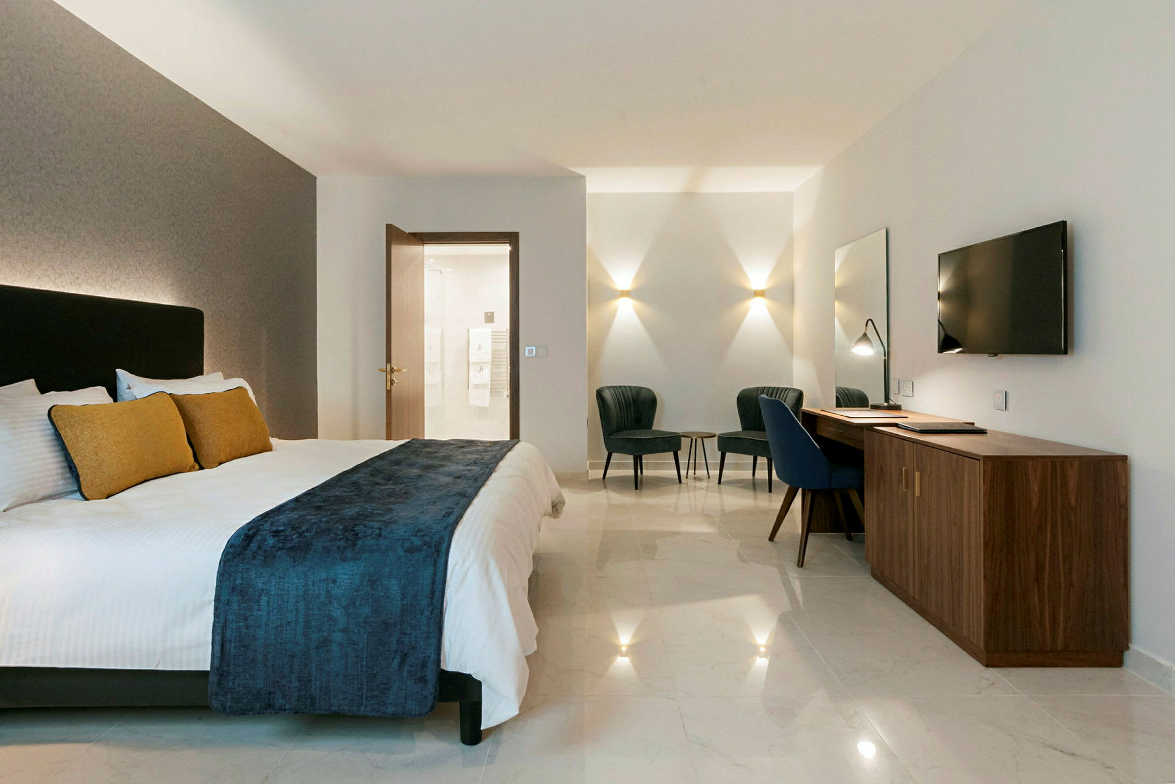 Hotellrum med dubbelsäng, skrivbord, två fåtöljer och väggmonterad TV. (AI-genererad text)
