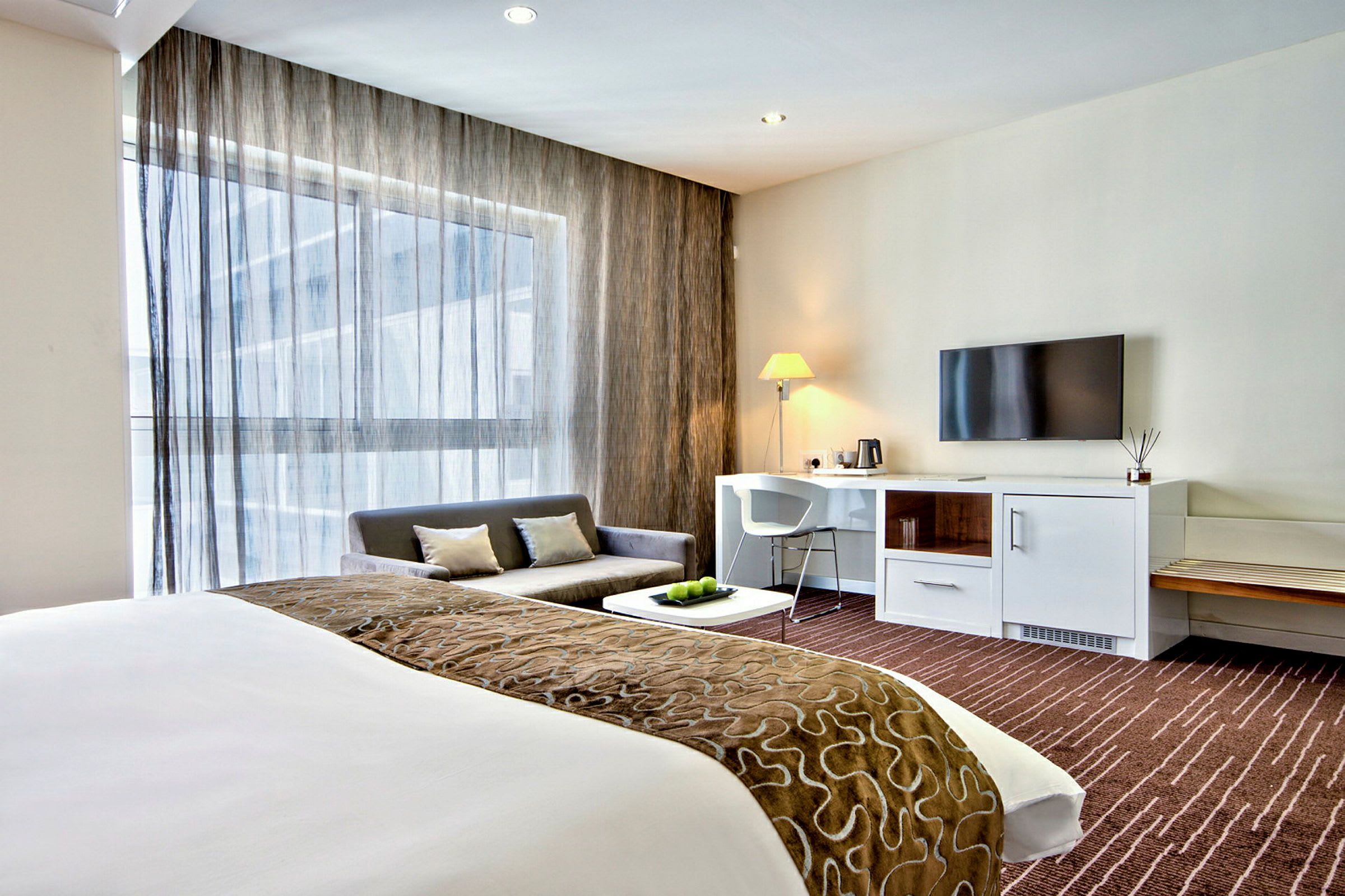 Ett modernt hotellrum med säng, soffa, skrivbord och TV. (AI-genererad text)