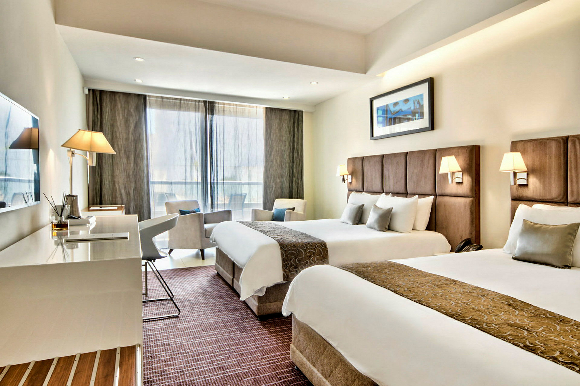 Hotellrum med två breda sängar, skrivbord, stolar och stora fönster. (AI-genererad text)