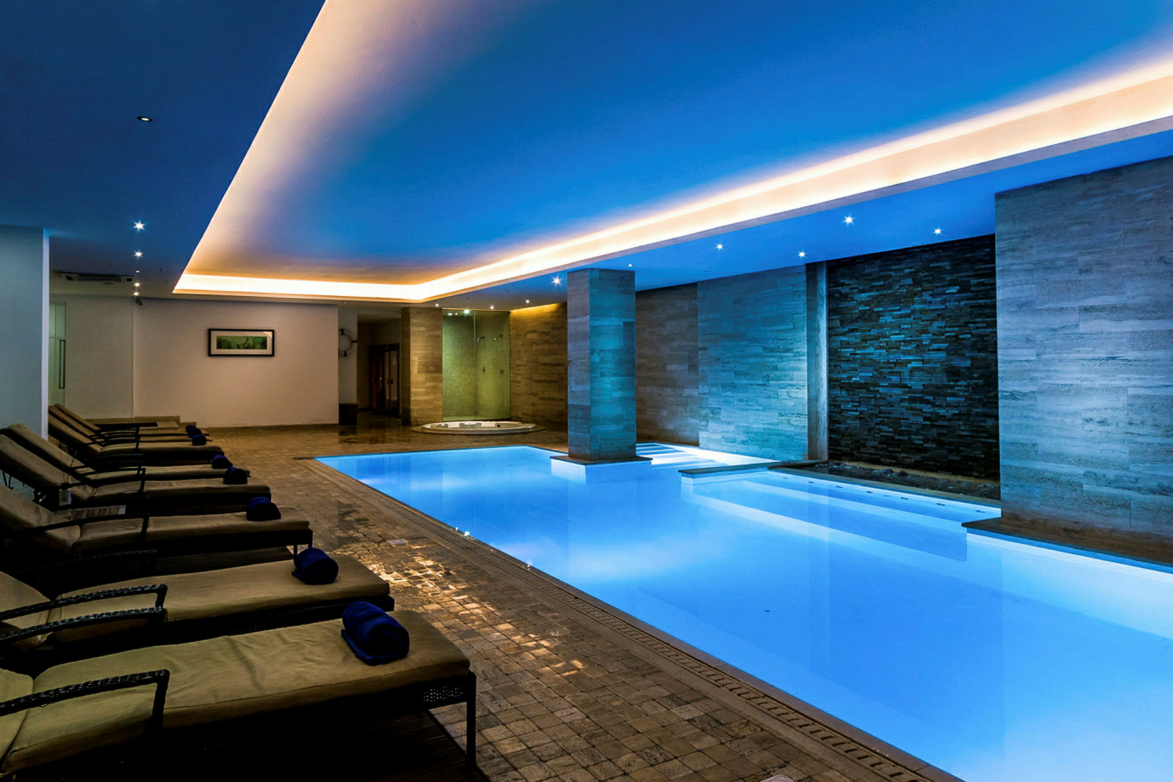 Bild av ett modernt inomhusspa med en upplyst swimmingpool, vilstolar och ett avkopplande atmosfär. (AI-genererad text)