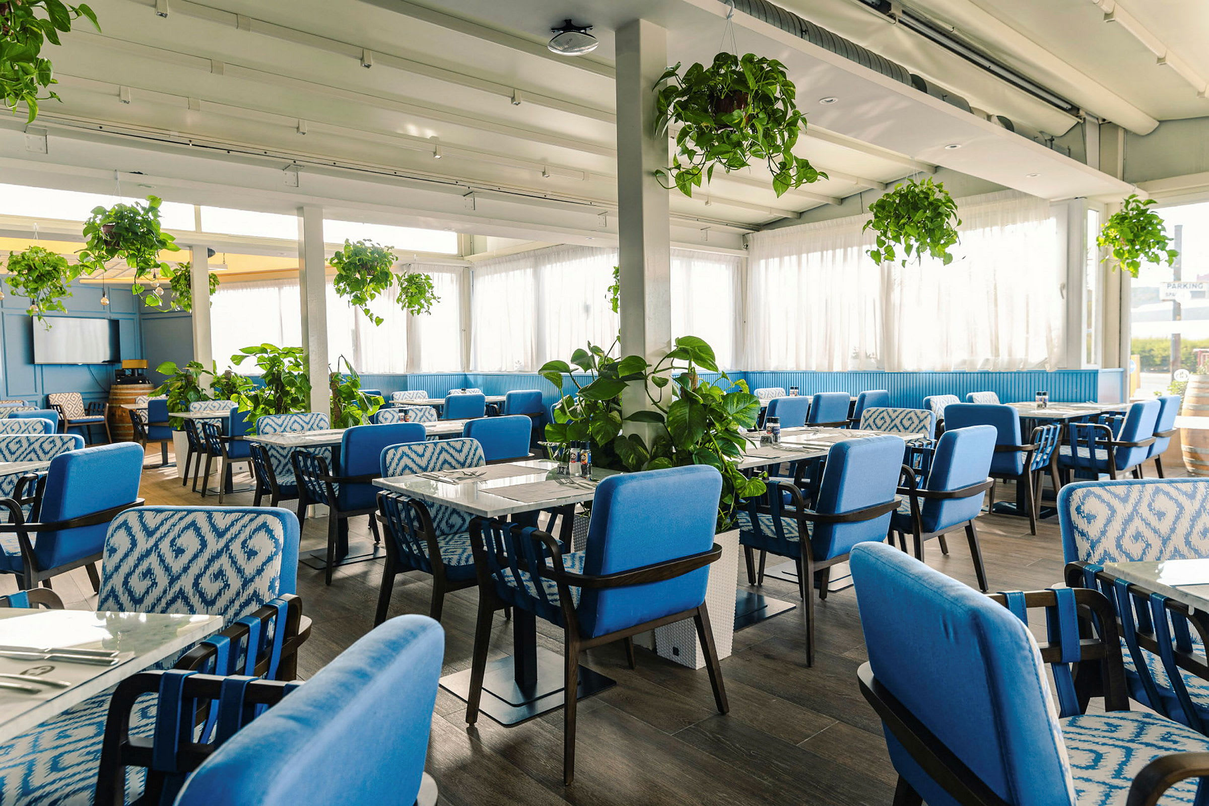 En restauranginteriör med blå stolar och gröna växter. (AI-genererad text)
