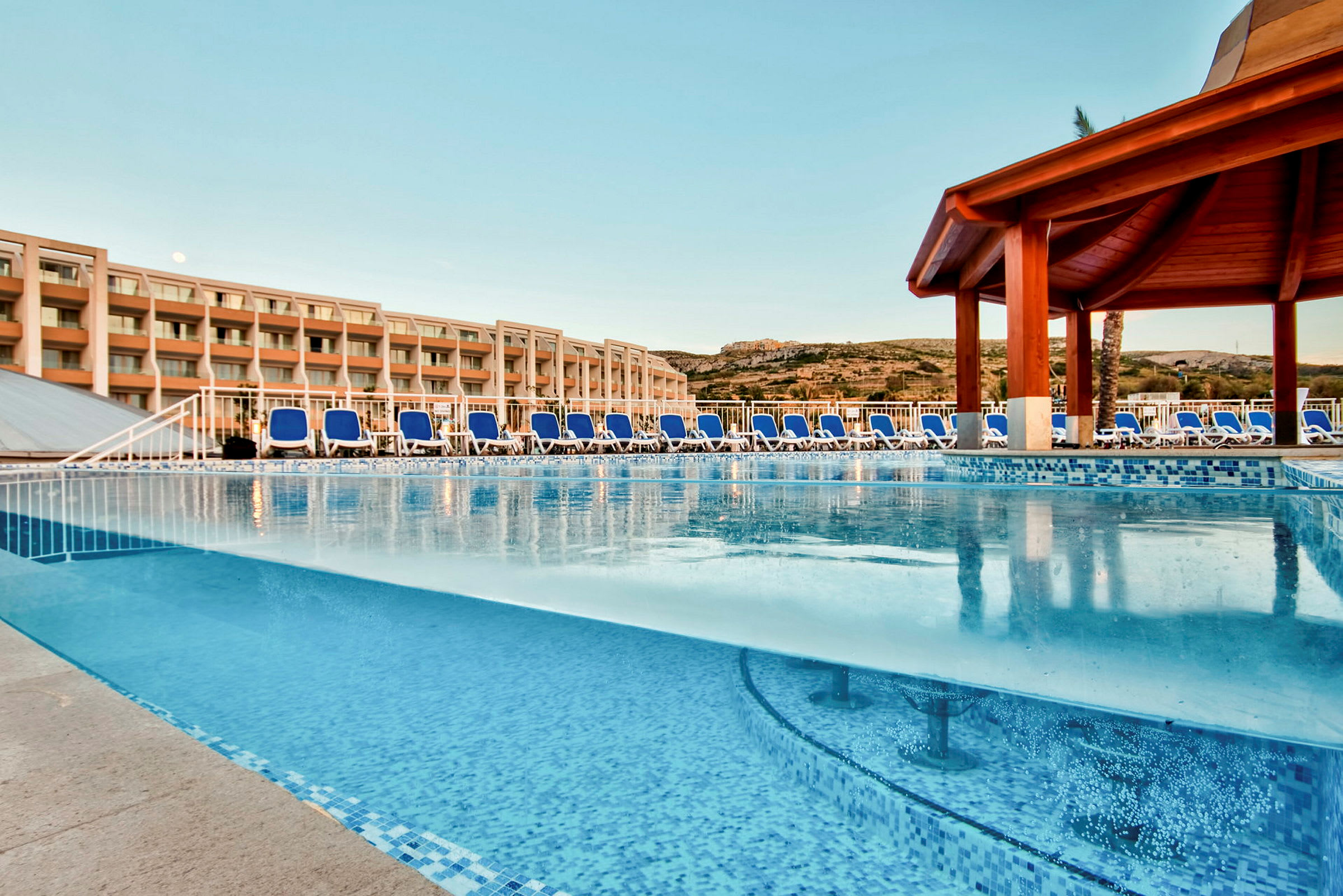 Utomhuspool med solstolar och hotellbyggnad i bakgrunden. (AI-genererad text)