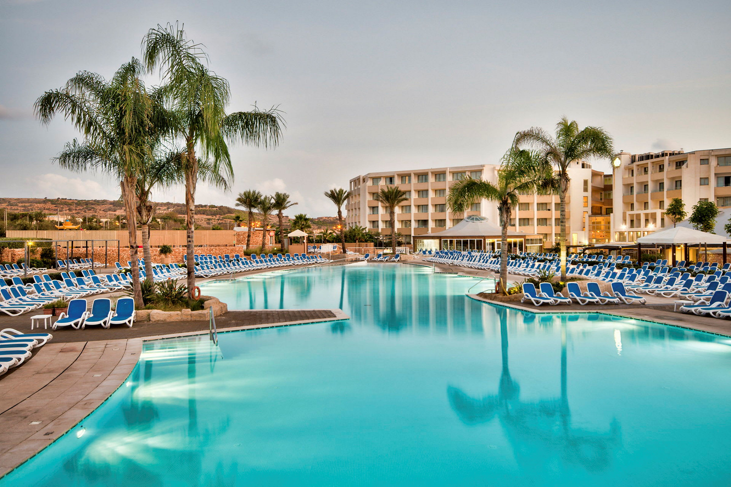 Stor pool med solstolar och palmer framför hotellbyggnader. (AI-genererad text)