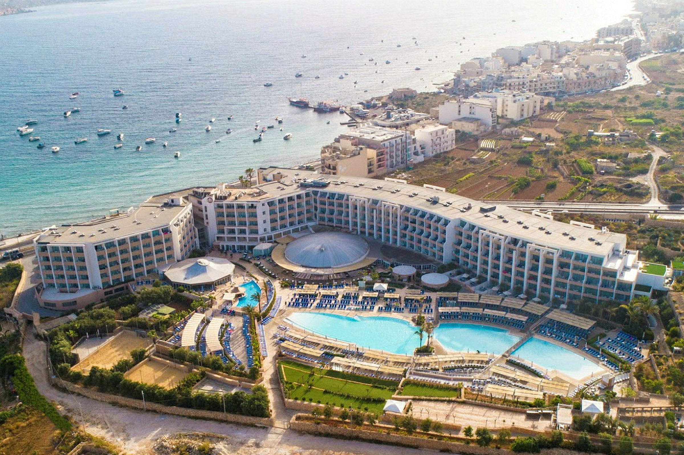 Flygfoto av ett hotellkomplex med pooler, grönområden och havsutsikt. (AI-genererad text)